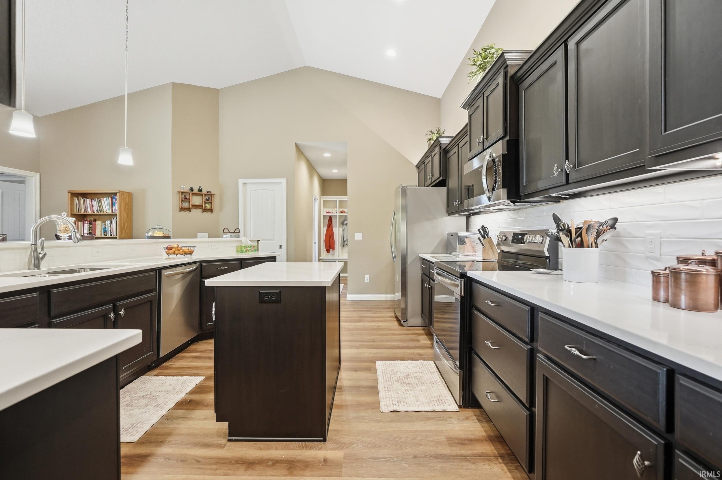 Modern kitchen featuring rich dark cabinetry, white countertops, stainless steel appliances, and wood-finish flooring