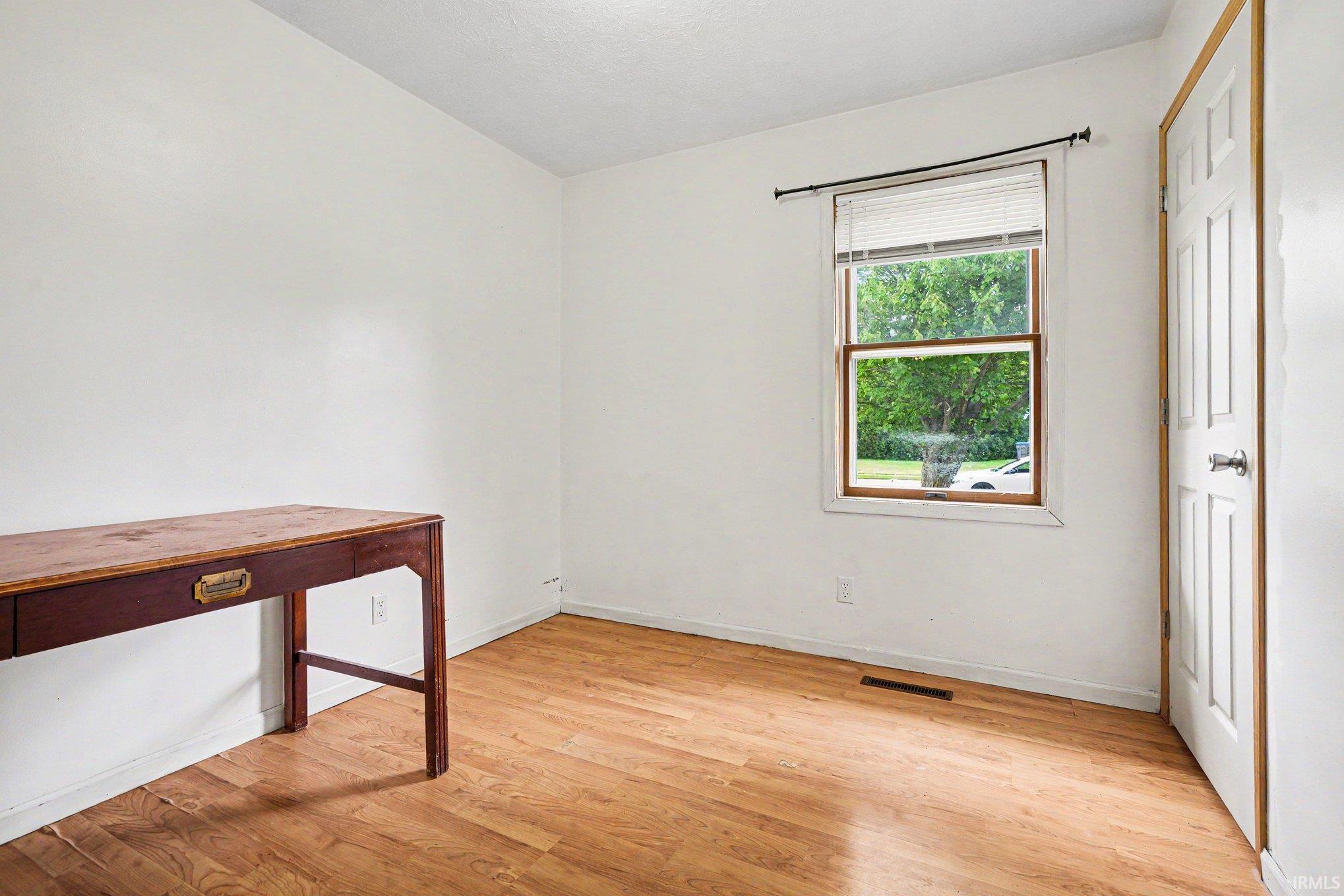 Bright room featuring wood-finish flooring, white walls, and a window with white blinds and wood trim