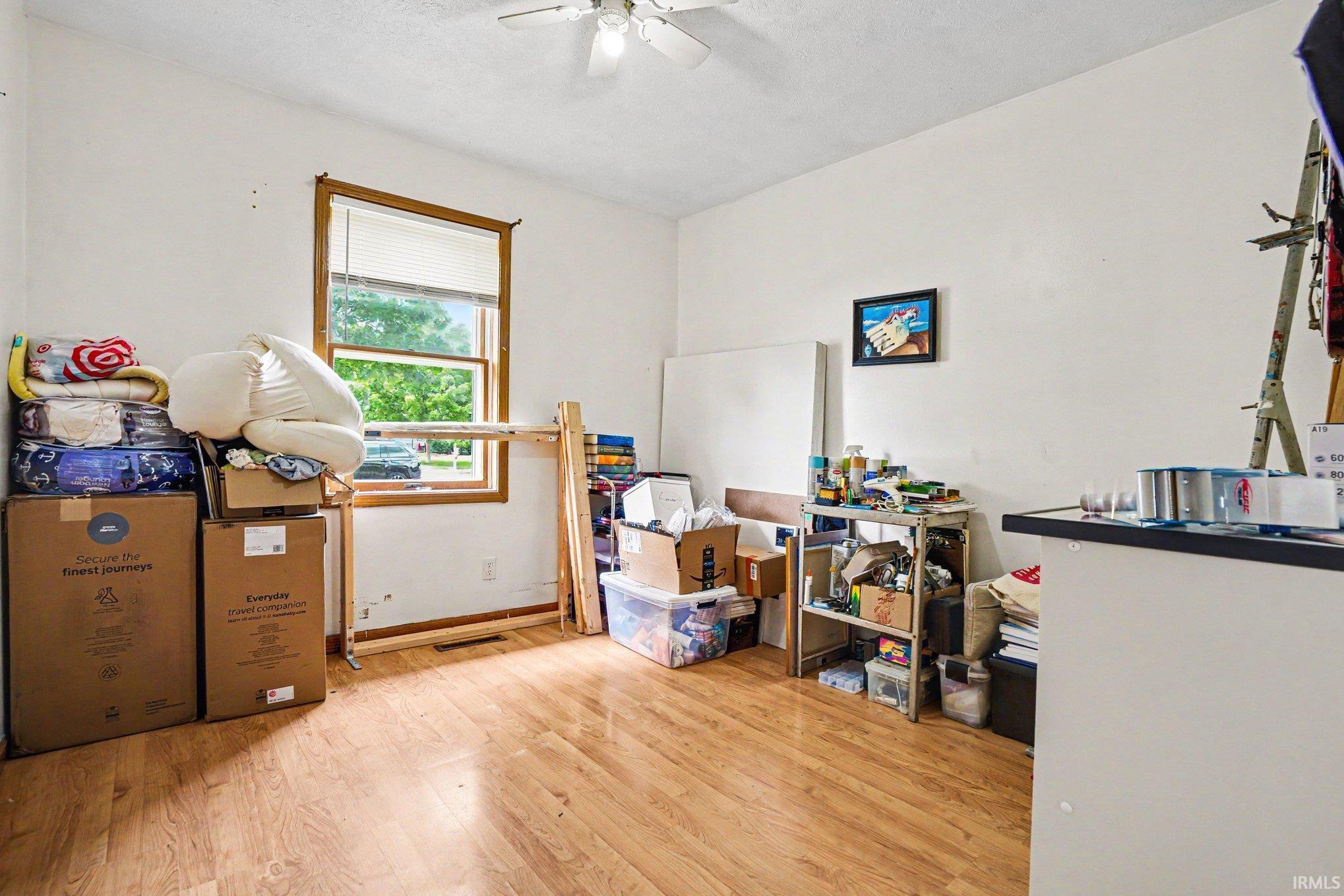 Room featuring wood-finish flooring, a ceiling fan, and a window with wood trim