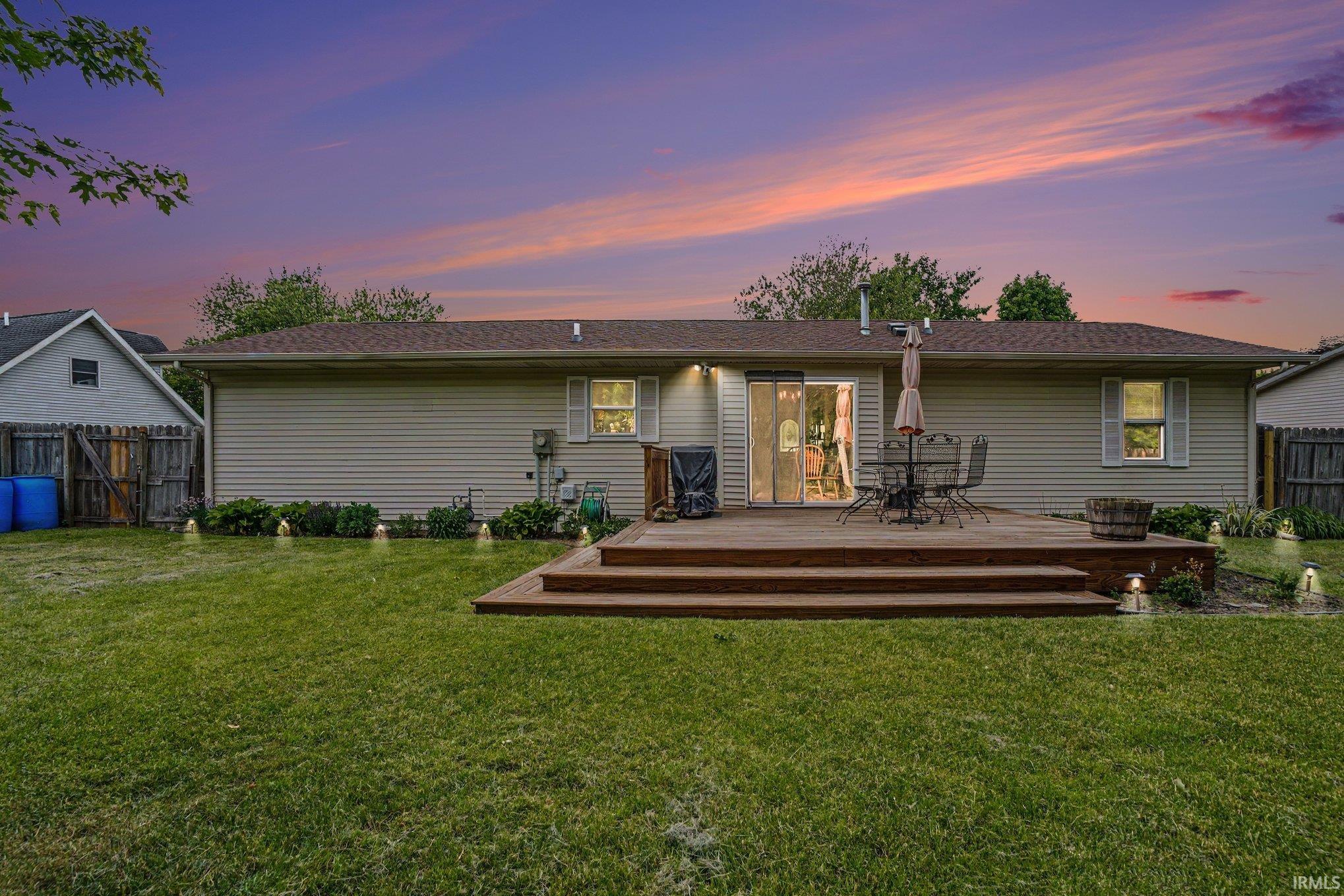 Spacious backyard featuring a multi-level wood deck, sliding glass door access, exterior lighting, and a manicured lawn