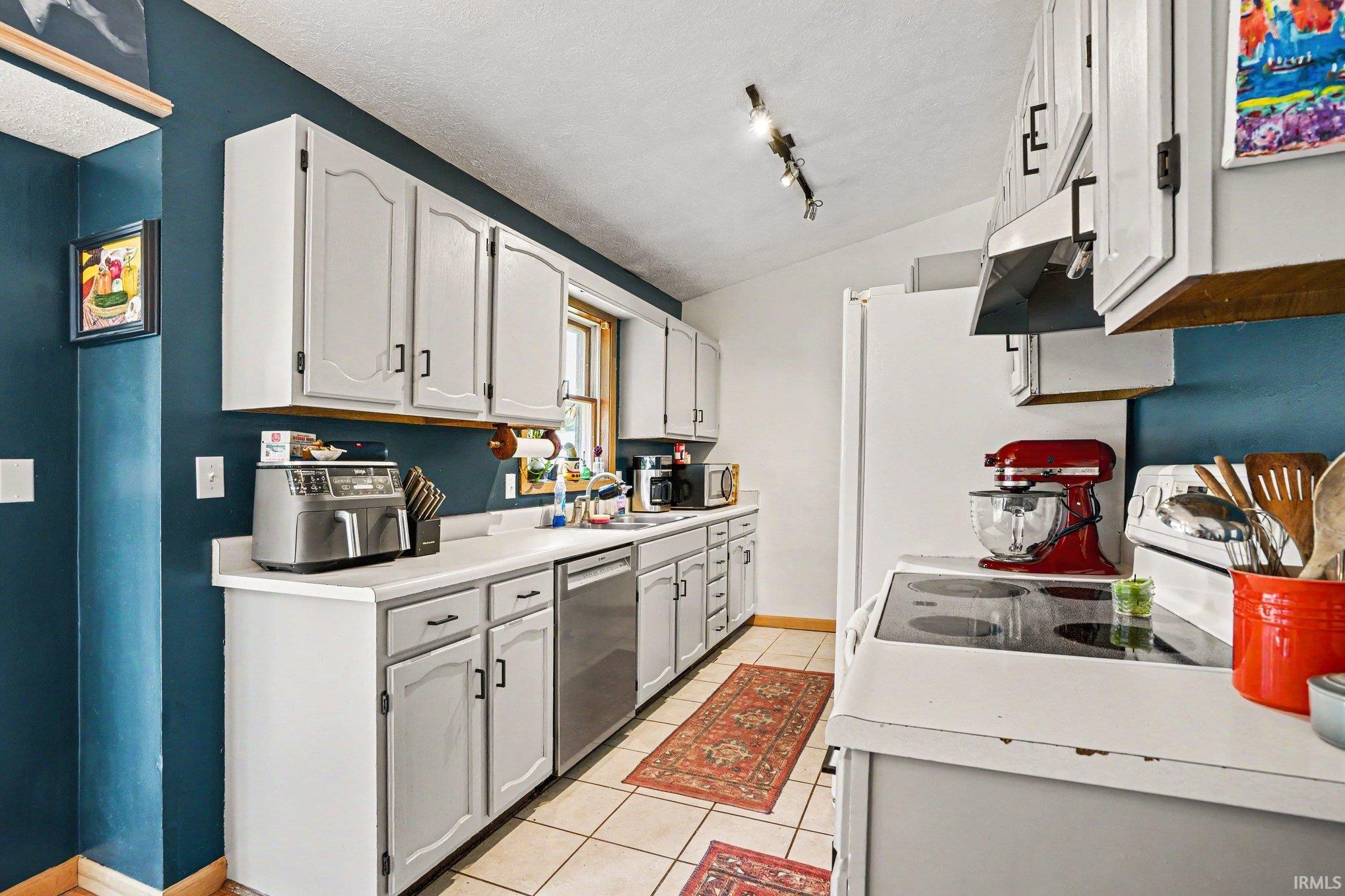 Kitchen featuring a window above the sink, light-toned cabinetry with dark hardware, a built-in dishwasher, and a range with an overhead hood