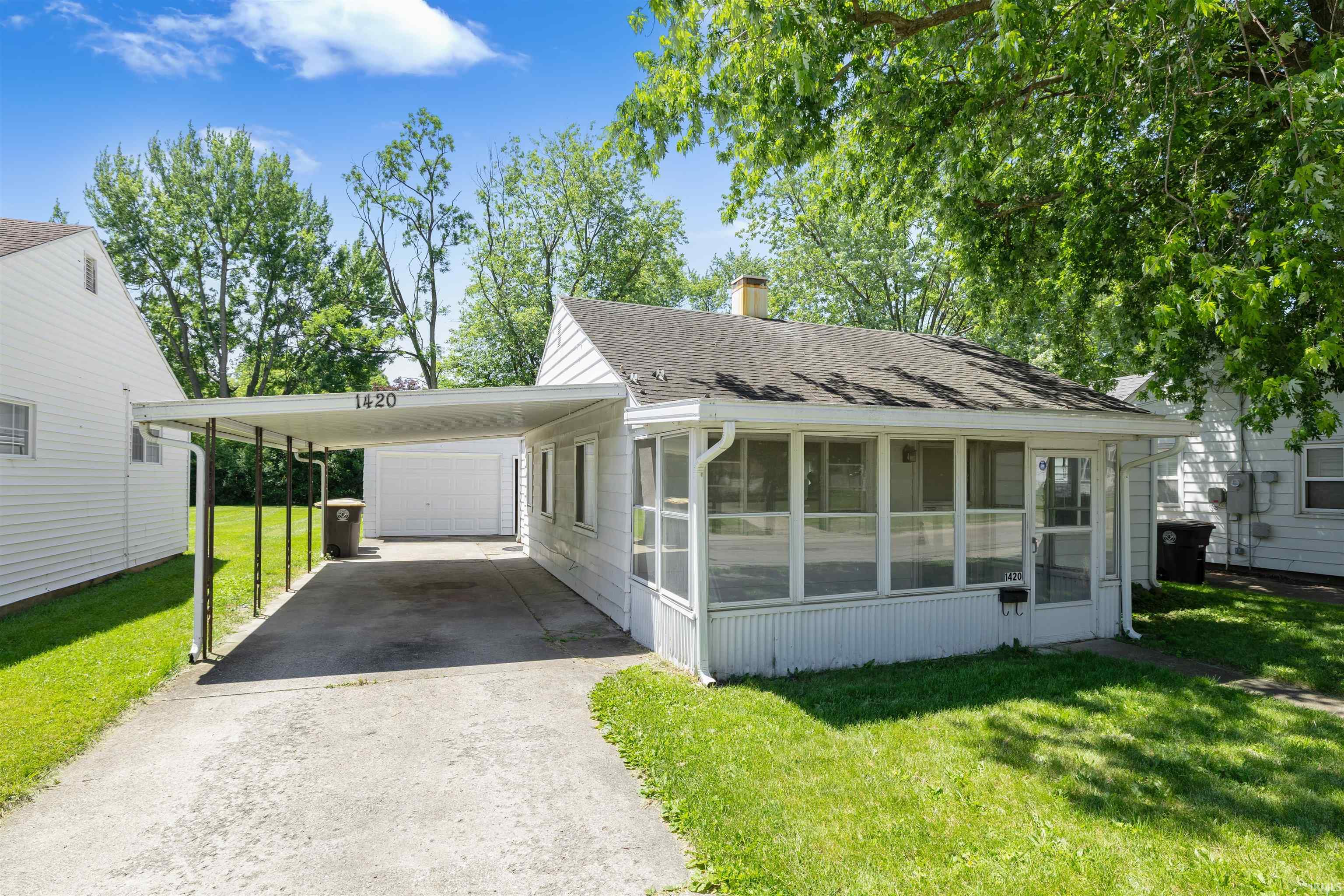 Single-story white siding residence featuring a screened-in porch, covered carport, and a detached garage