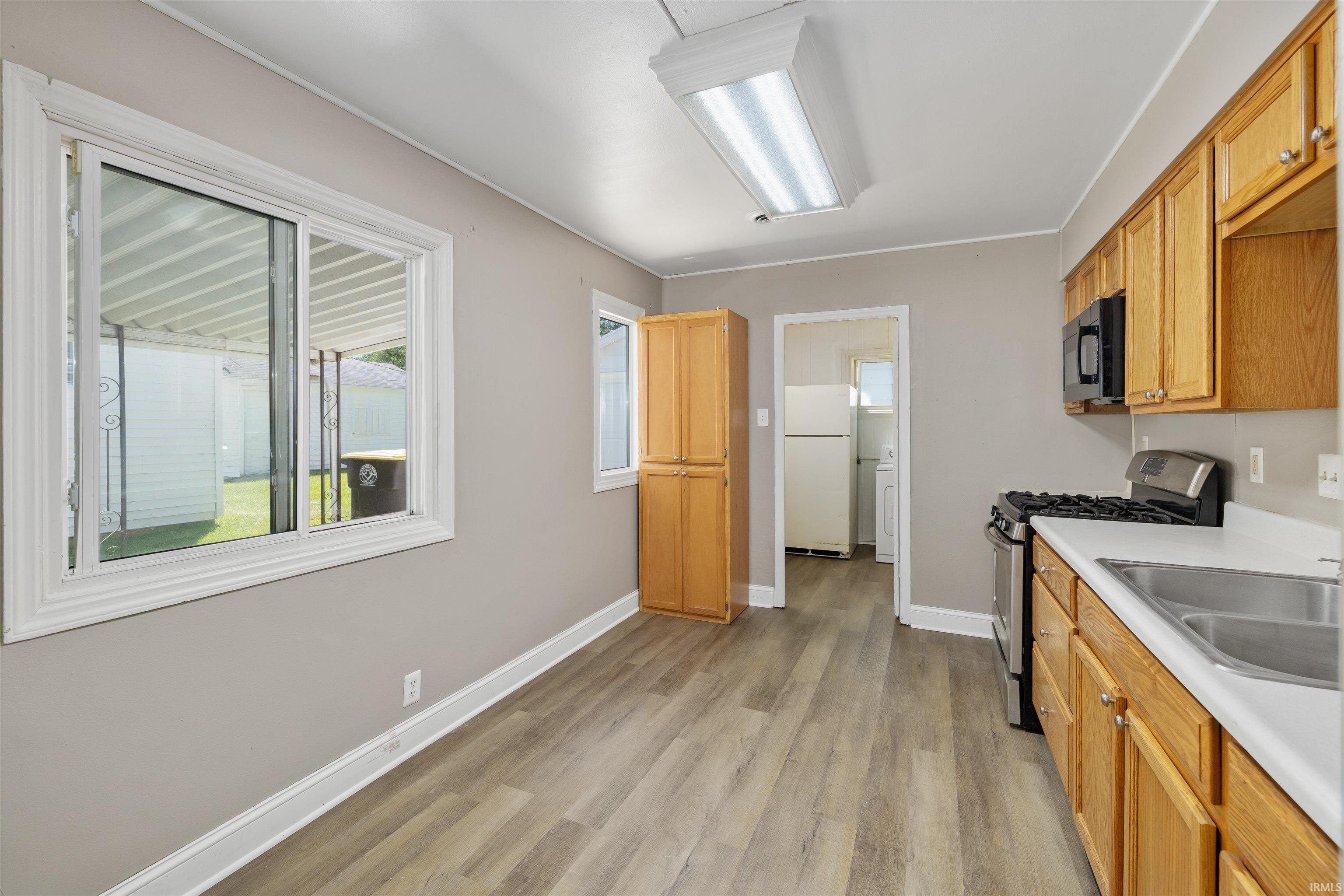 Kitchen featuring wood-finish flooring, warm-toned cabinetry, stainless steel sink, and a black microwave