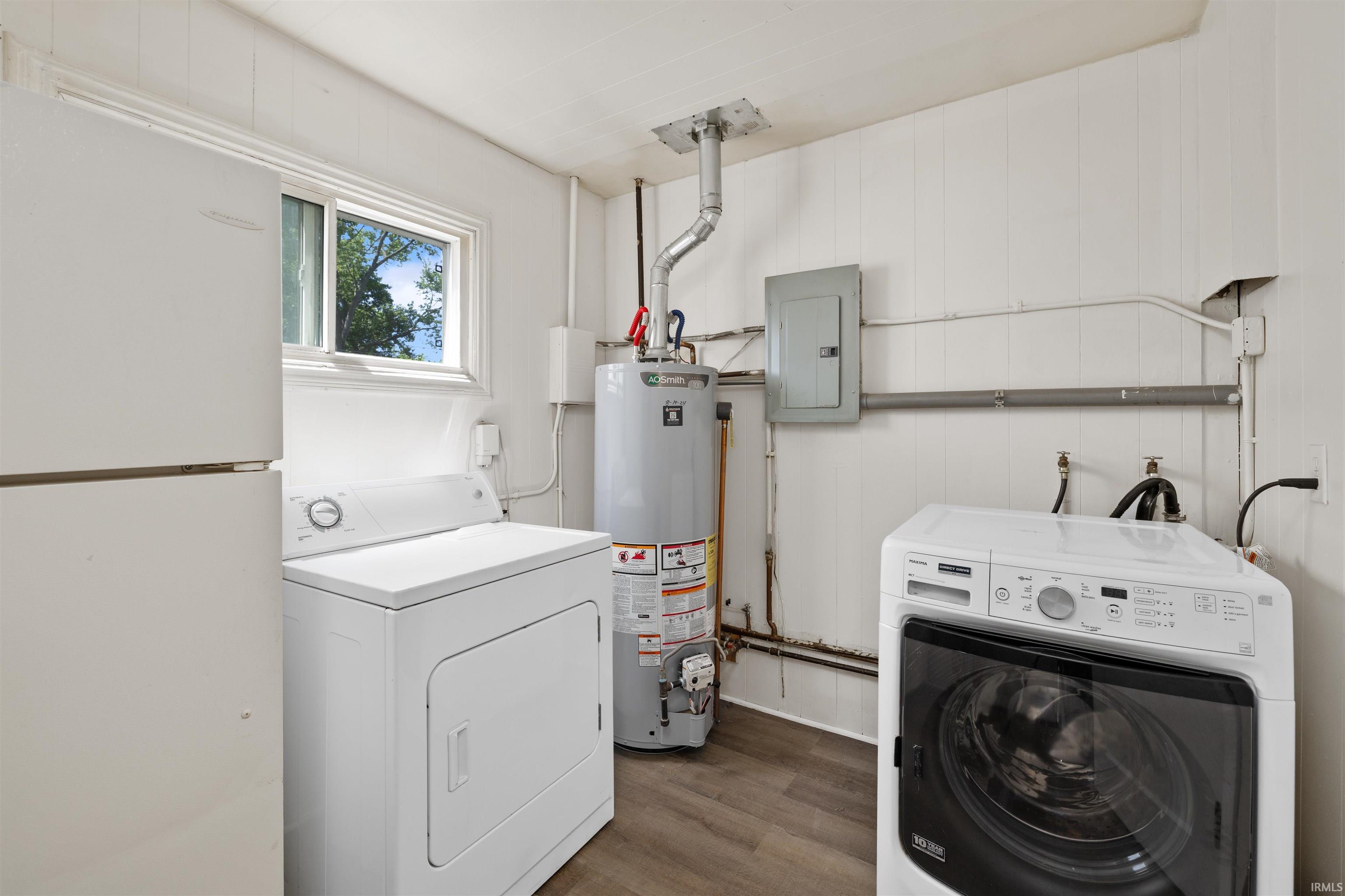 Utility room featuring a water heater, electrical panel, and wood-finish flooring