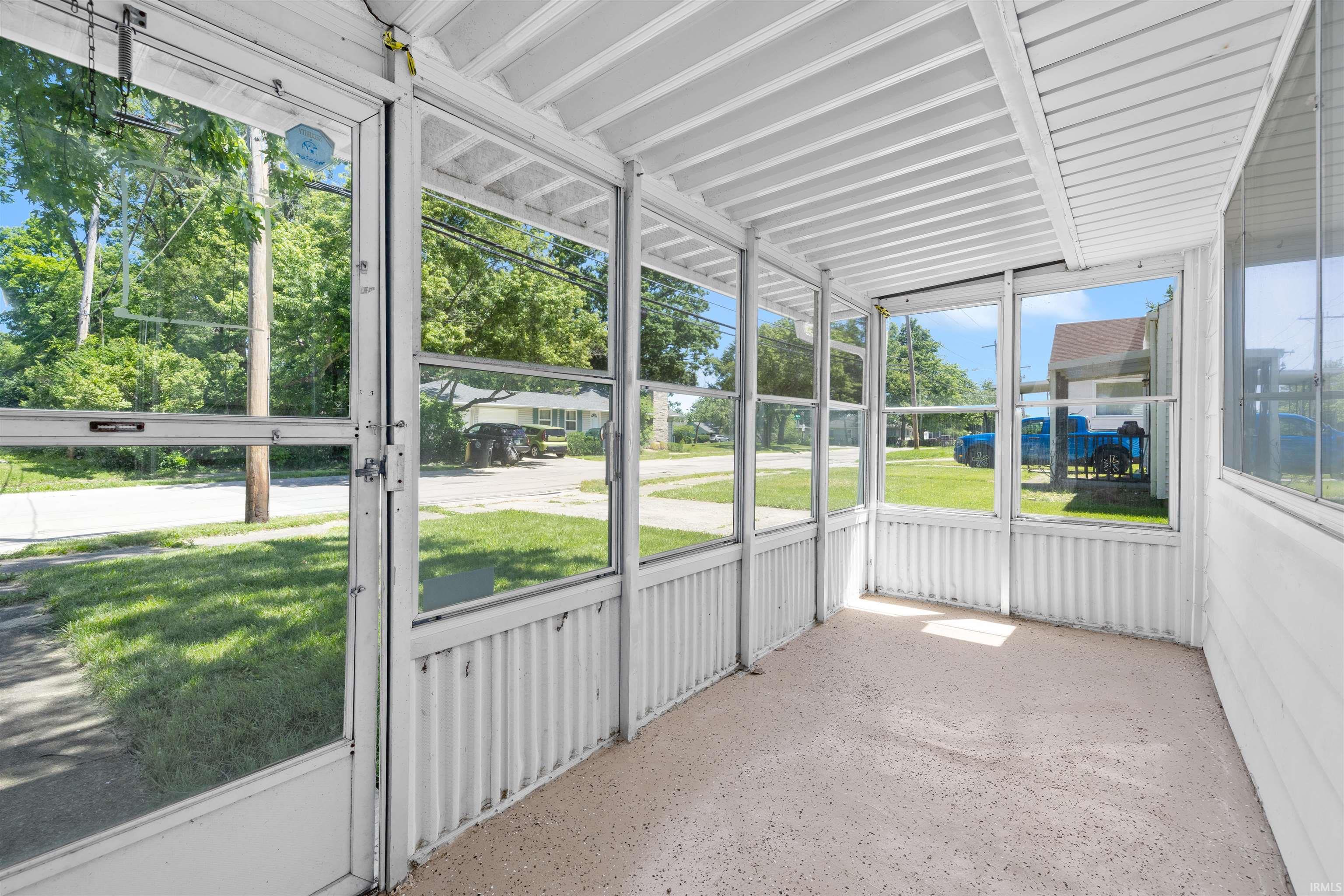 Enclosed porch featuring multiple large windows, textured white walls, a white slatted ceiling, and a light-colored speckled flooring