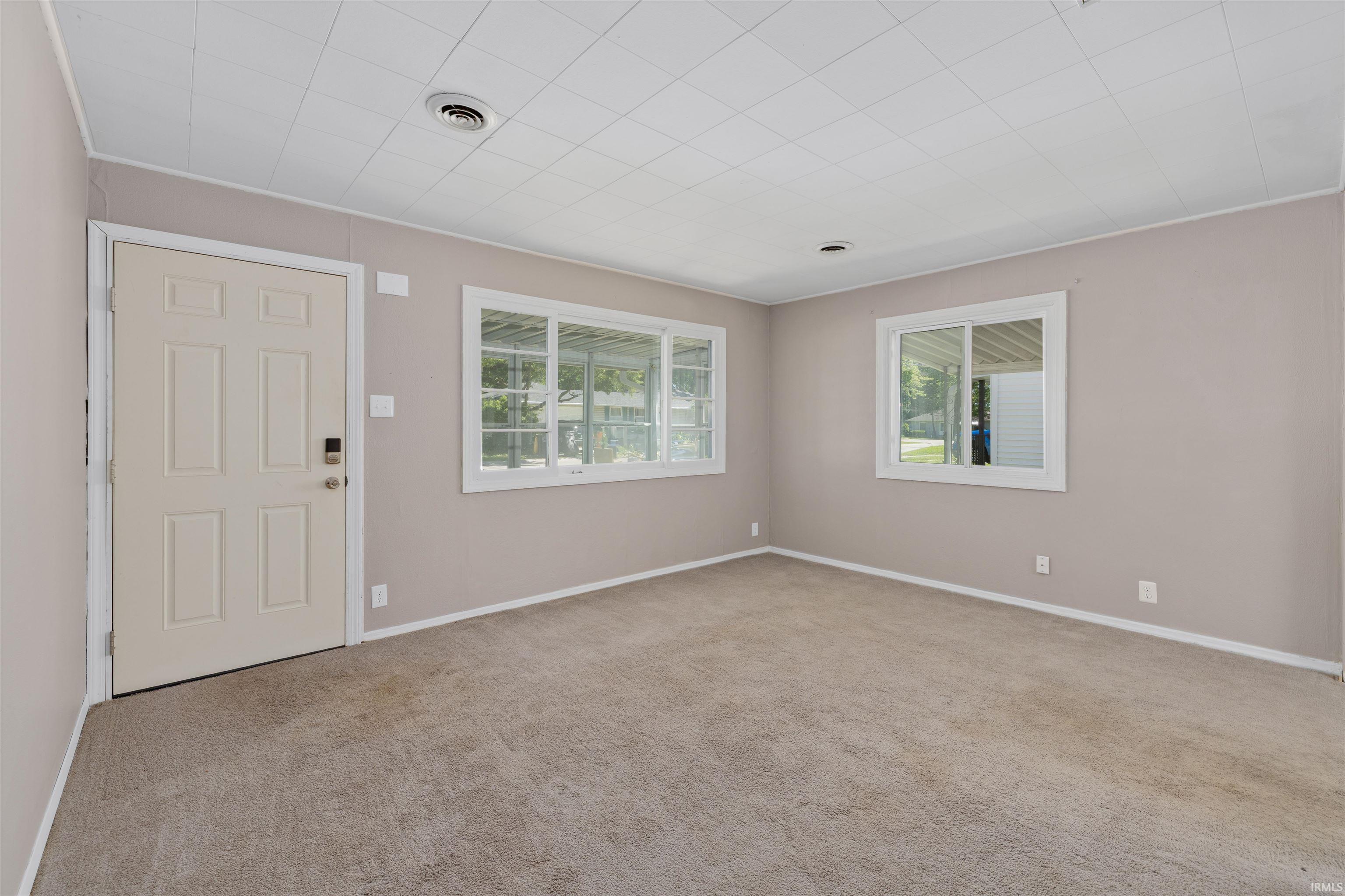 Carpeted interior space featuring a paneled entry door with smart lock, two windows with white trim, light-toned walls, and a textured ceiling
