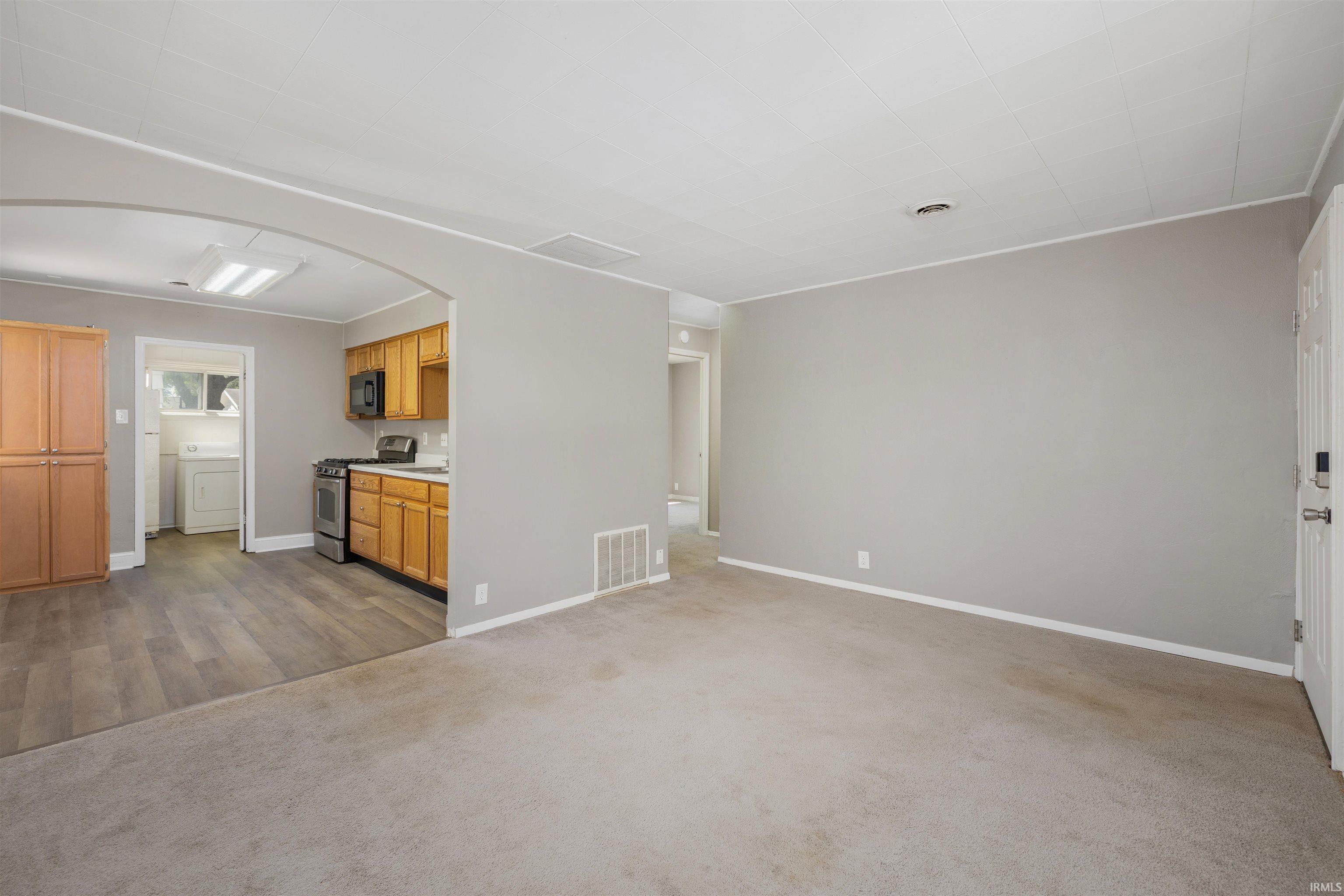 Open concept interior featuring a carpeted living area, arched doorway, and wood-finish flooring