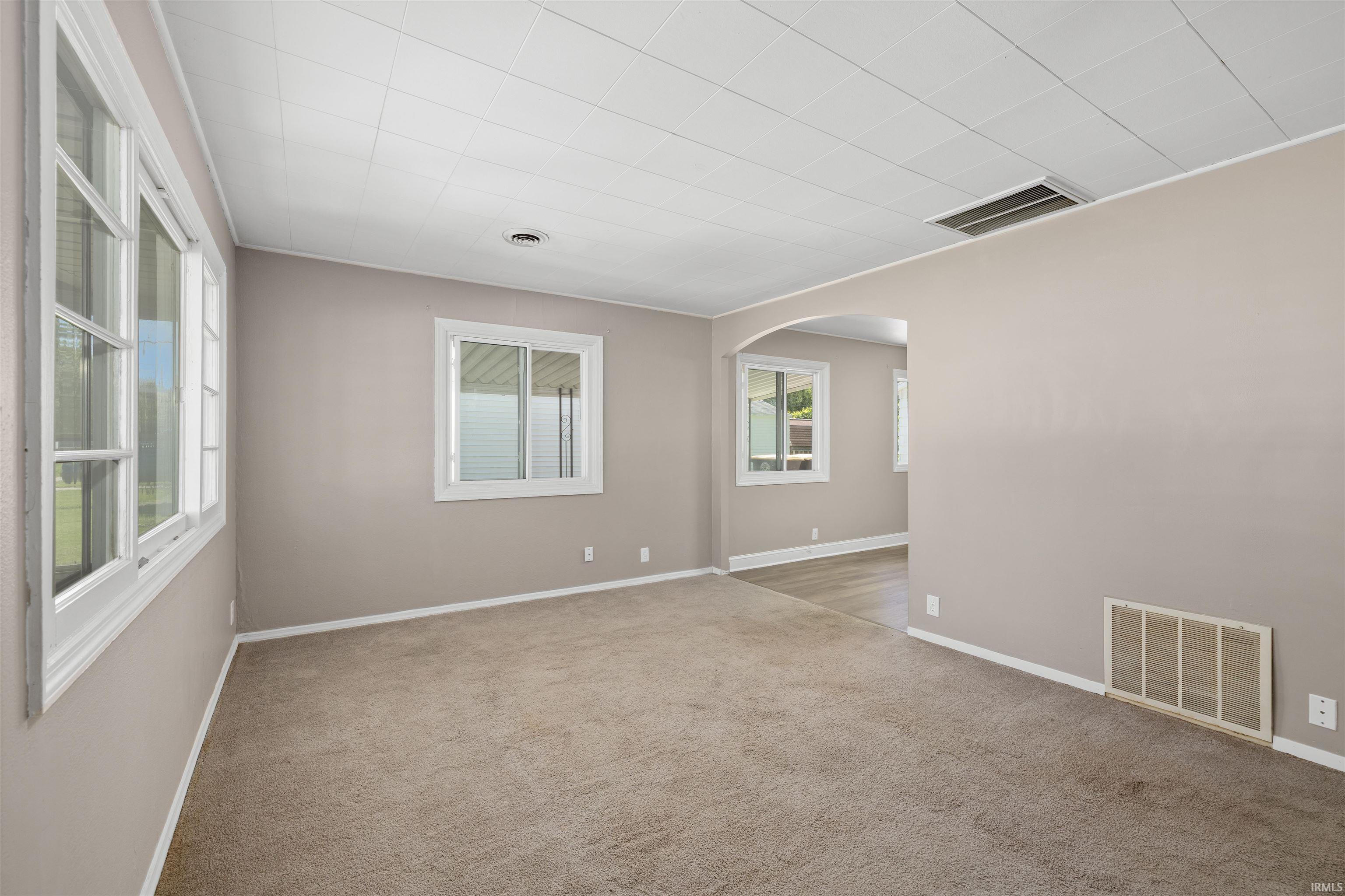 Spacious room featuring neutral wall tones, light-colored carpeting, multiple windows, and a white ceiling with recessed lighting