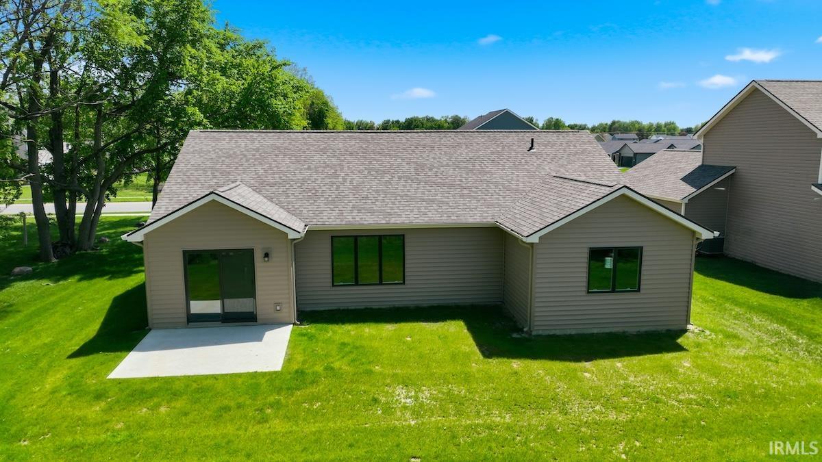 Back exterior featuring tan horizontal siding, a gray asphalt shingle roof, and a concrete patio