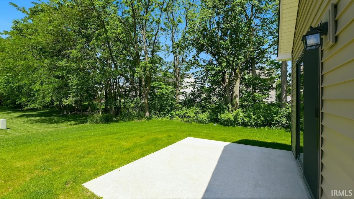 Expansive green lawn featuring a concrete patio, mature trees, exterior wall siding, and a sliding glass door