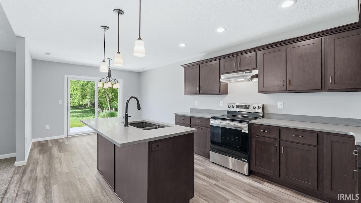 Modern kitchen featuring dark wood cabinetry, light countertops, stainless steel appliances, and a central island with an undermount sink