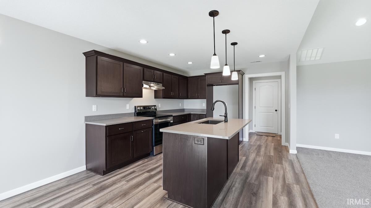 Kitchen featuring dark wood cabinetry, light countertops, wood-finish flooring, stainless steel appliances, and an island with pendant lighting