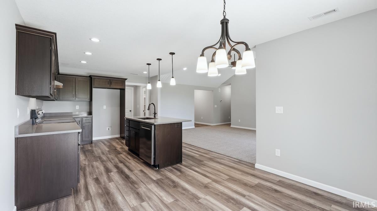 Open concept kitchen featuring dark wood cabinetry, stainless steel appliances, a central island with a sink, and wood-finish flooring