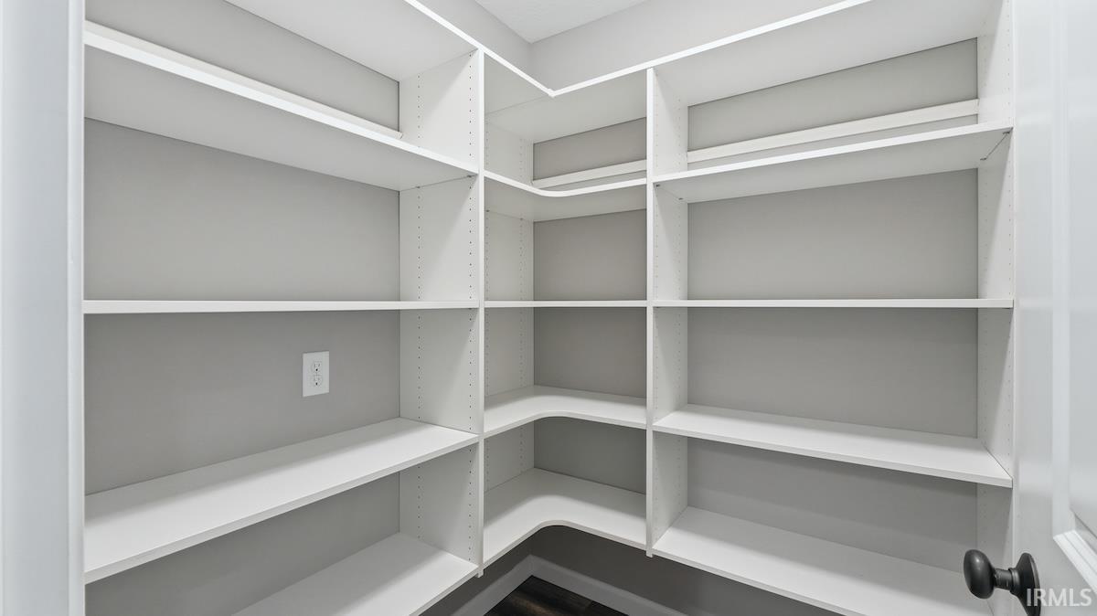 Expansive custom shelving system with white adjustable shelves and corner units, dark wood-finish flooring, and a matte black door knob