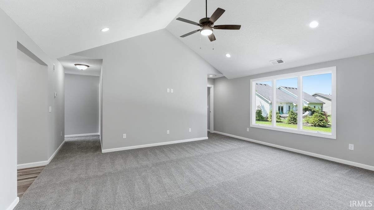 Spacious room featuring vaulted ceilings, recessed lighting, a ceiling fan, large window, and light gray carpeting
