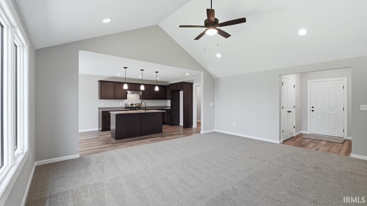 Spacious open-concept living area featuring vaulted ceilings, recessed lighting, and a ceiling fan