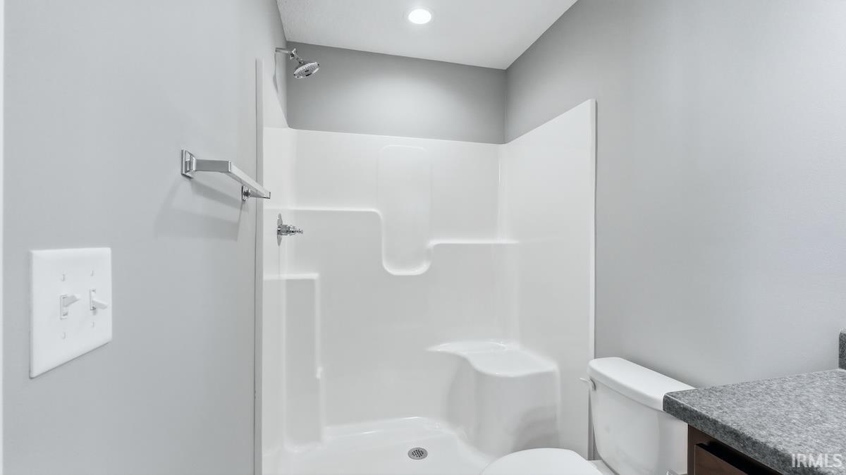 Bathroom featuring a white shower stall with built-in seating, a chrome shower head and faucet, a white toilet, and a vanity with a dark countertop