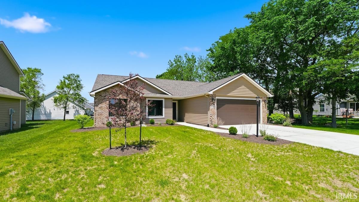 Modern ranch-style home featuring a two-car garage, partial stone facade, beige siding, and a well-maintained front lawn with young trees