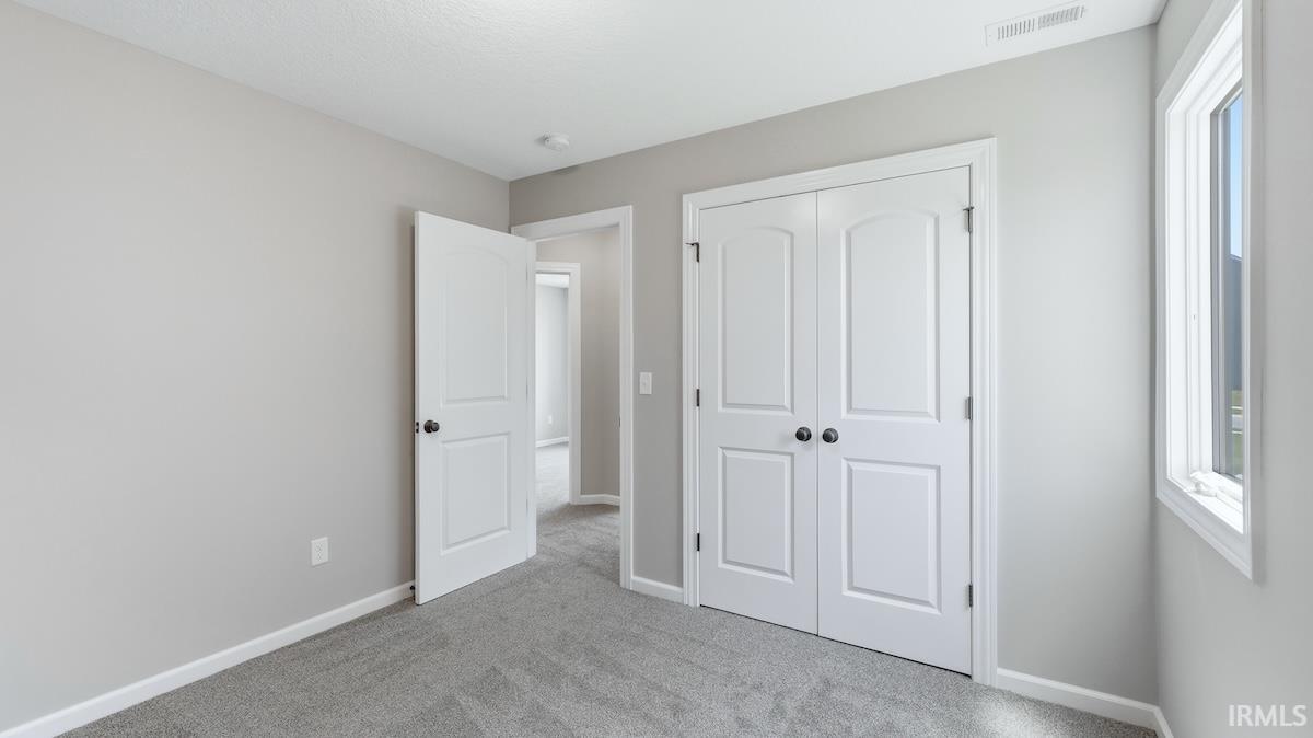 Room featuring neutral wall tones, gray carpeting, a double-door closet with black hardware, and a single window with white trim