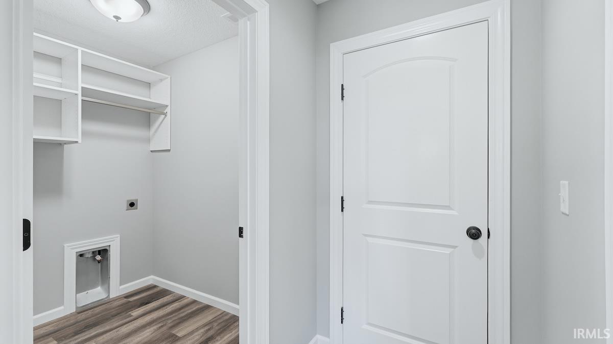 Dedicated laundry area featuring built-in white shelving, a hanging rod, and wood-finish flooring