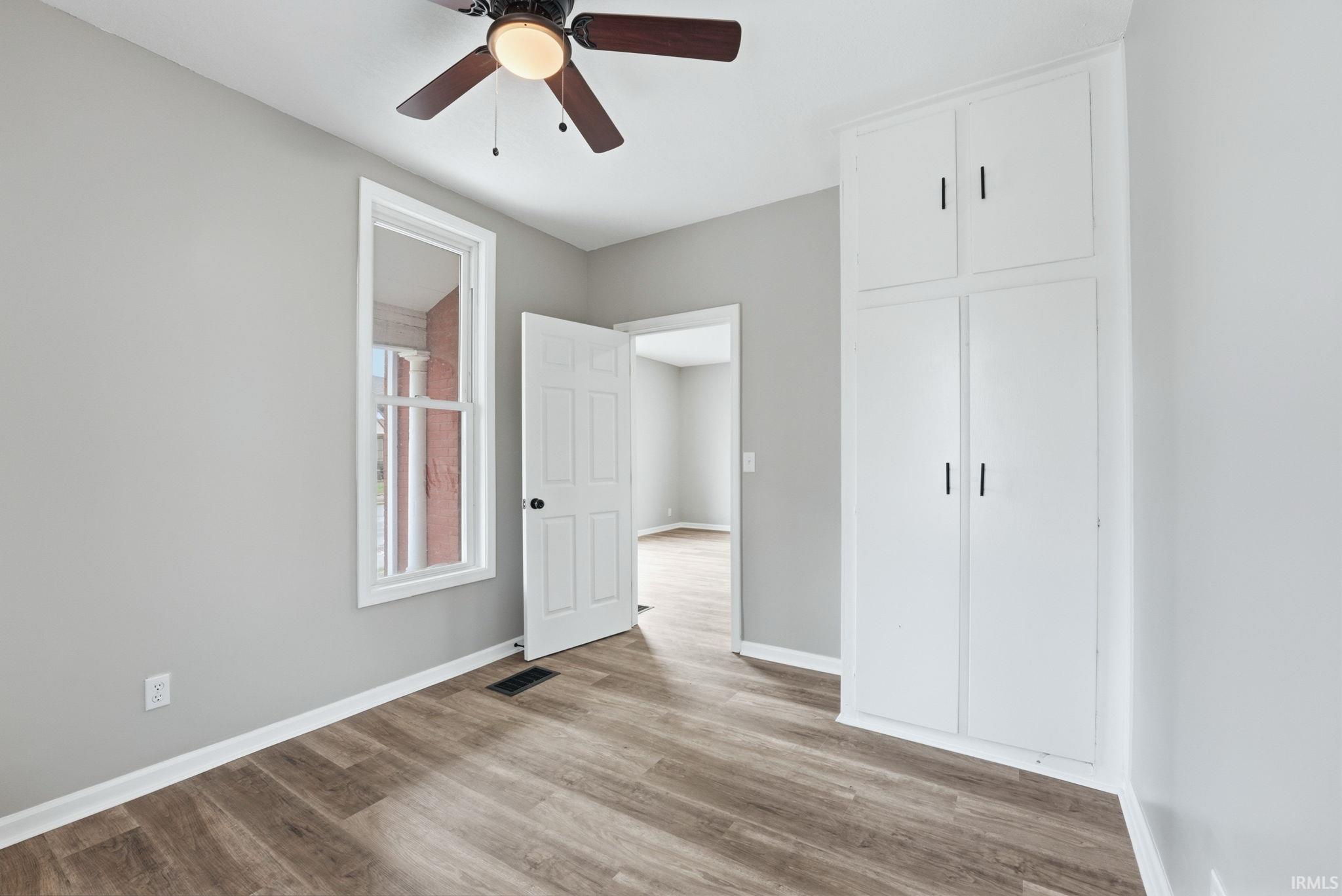Bedroom featuring wood-finish flooring, built-in cabinetry, a ceiling fan, and a single window with white trim