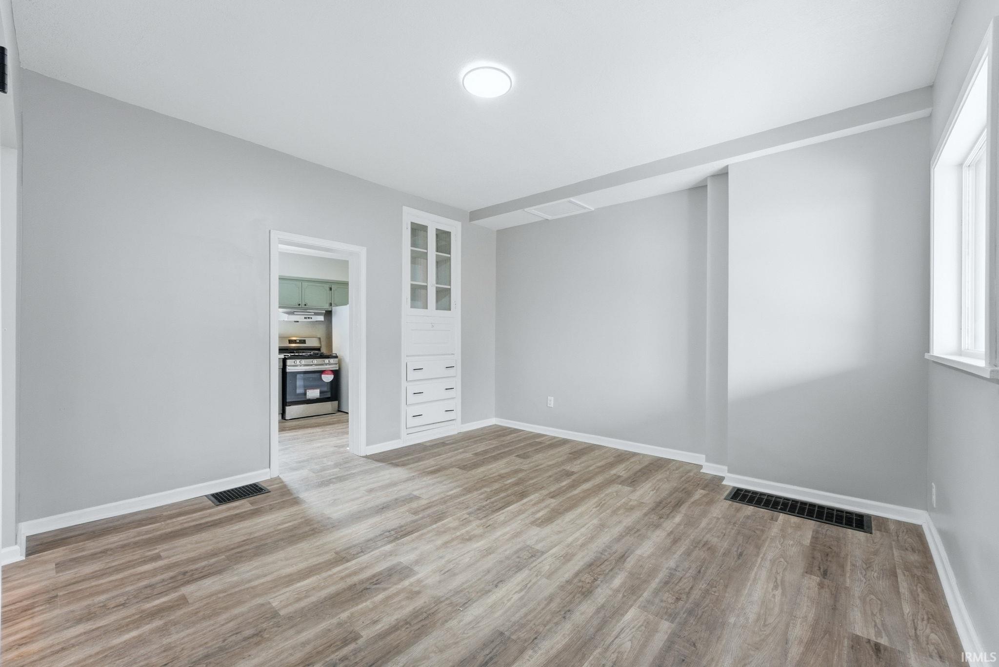 Bright interior space featuring wood-finish flooring, light gray walls, white trim, and a built-in cabinet with glass-front uppers