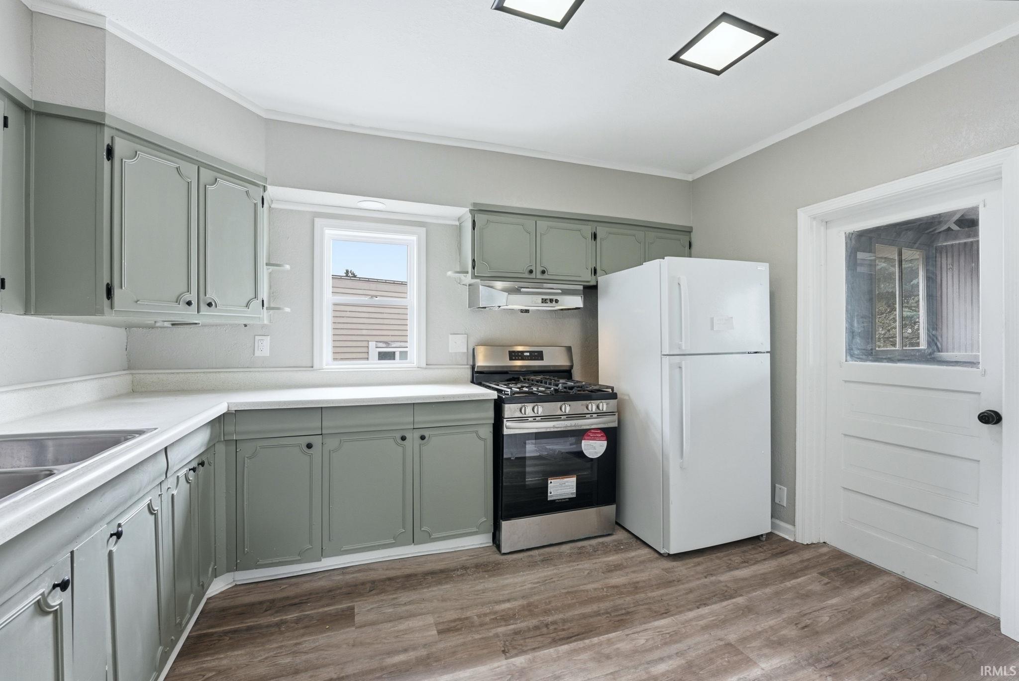 Kitchen featuring sage green cabinetry with black hardware, white countertops, wood-finish flooring, a stainless steel range, and a white refrigerator