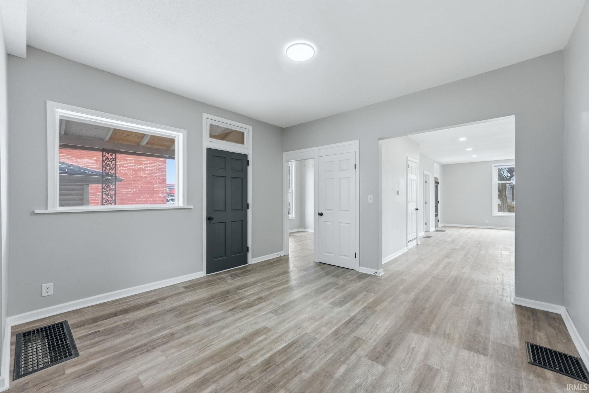 Spacious interior featuring wood-finish flooring, light grey painted walls, white trim, and a dark paneled door with transom window