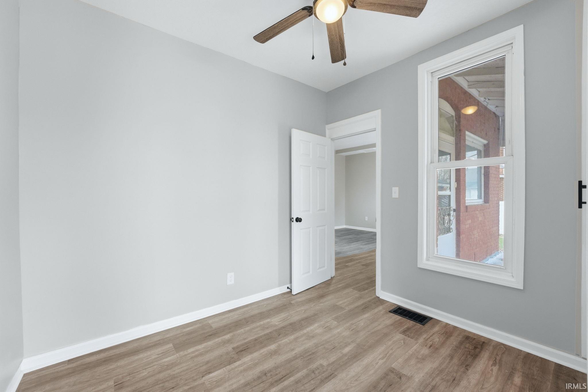 Room featuring wood-finish flooring, light gray walls, white trim, and a ceiling fan with integrated lighting
