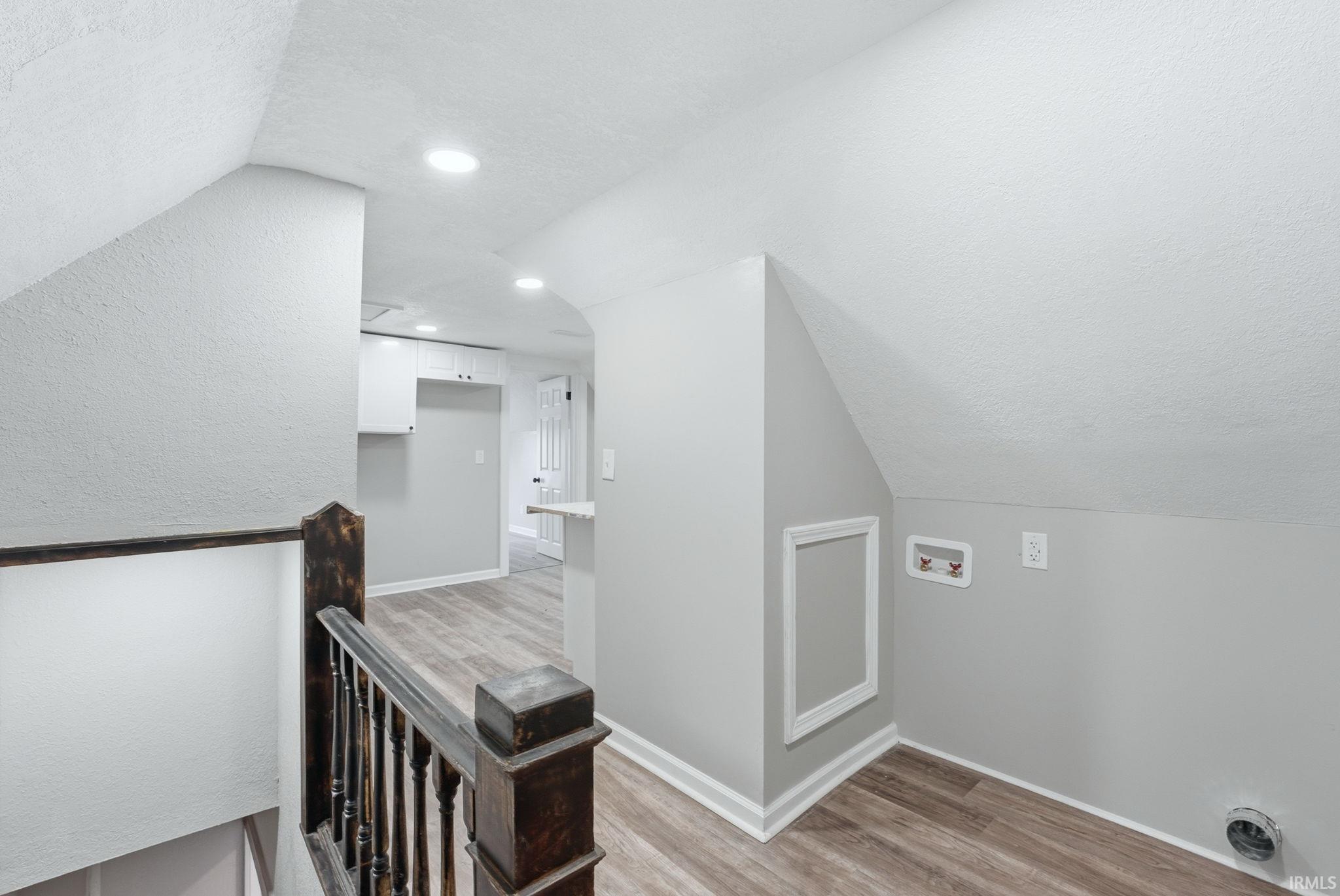 Upper-level landing featuring wood-finish flooring, recessed lighting, and a dark wood banister