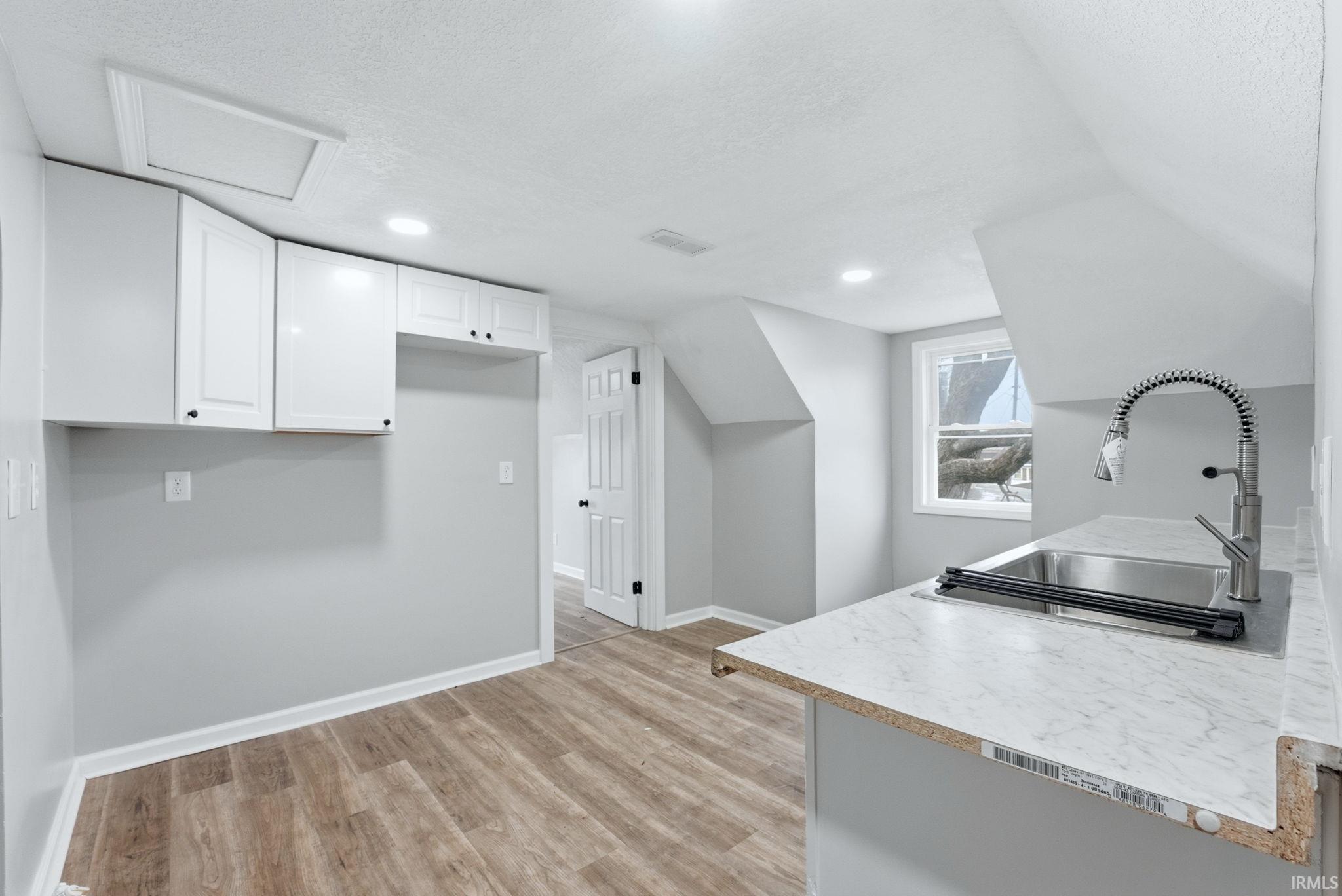 Kitchenette featuring wood-finish flooring, white cabinetry, recessed lighting, and a stainless steel sink with a modern pull-down faucet