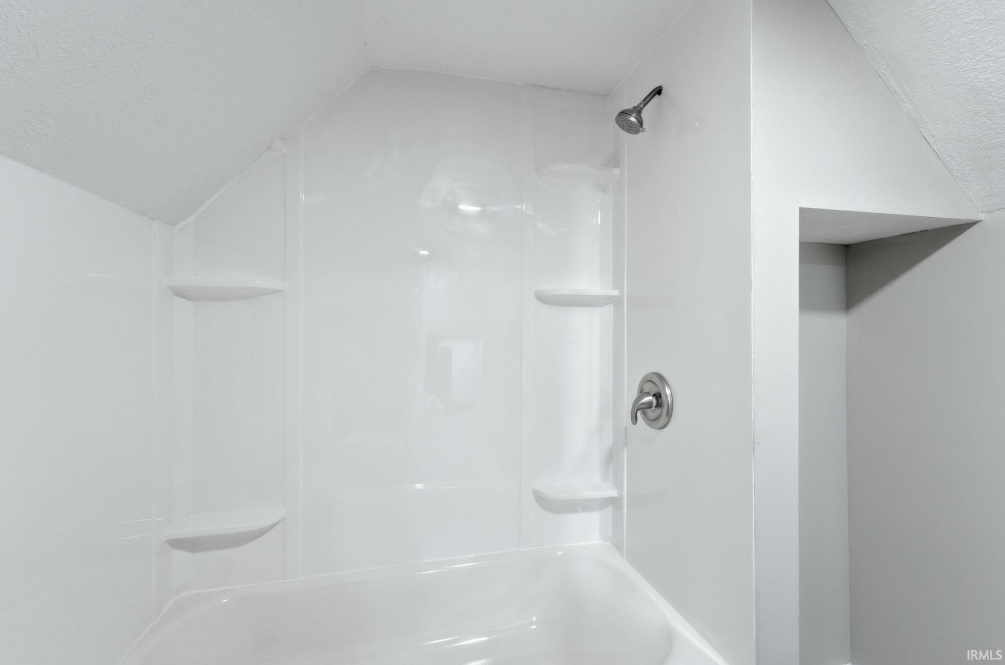 Integrated white shower/tub unit featuring a chrome shower head and control, built-in shelving, and a clean, bright finish