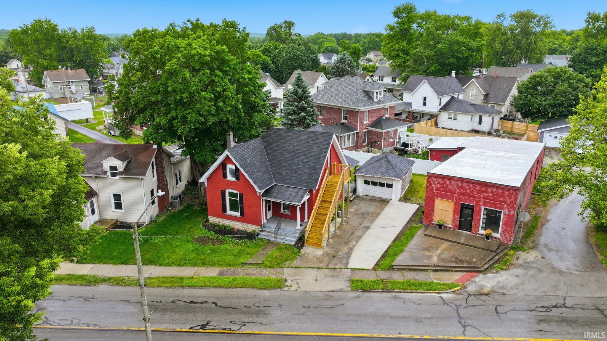 Red exterior home with contrasting white trim, featuring a detached garage, a separate commercial-style building, and mature surrounding trees