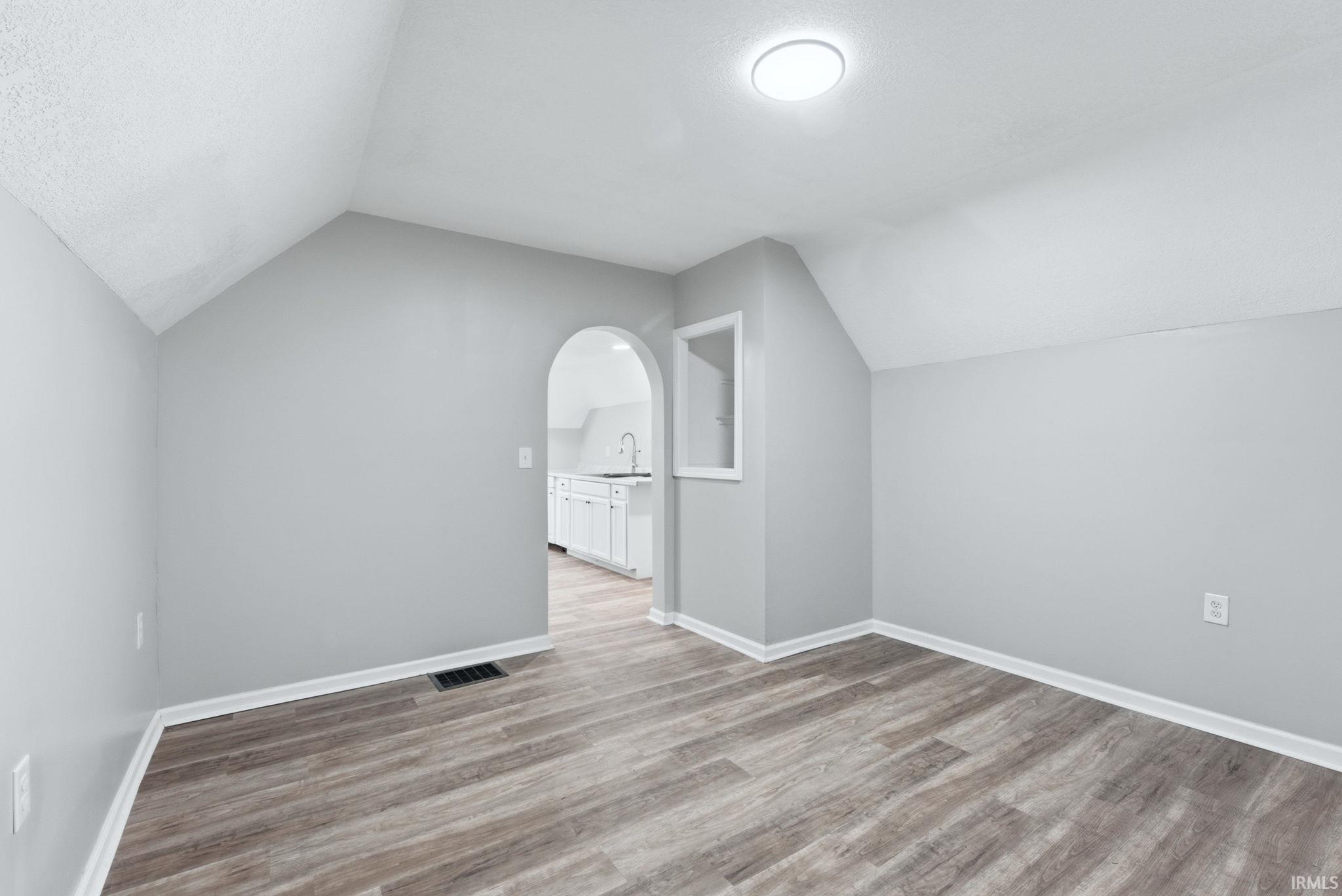 Room featuring light gray walls, wood-finish flooring, a contemporary ceiling light fixture, and an arched doorway