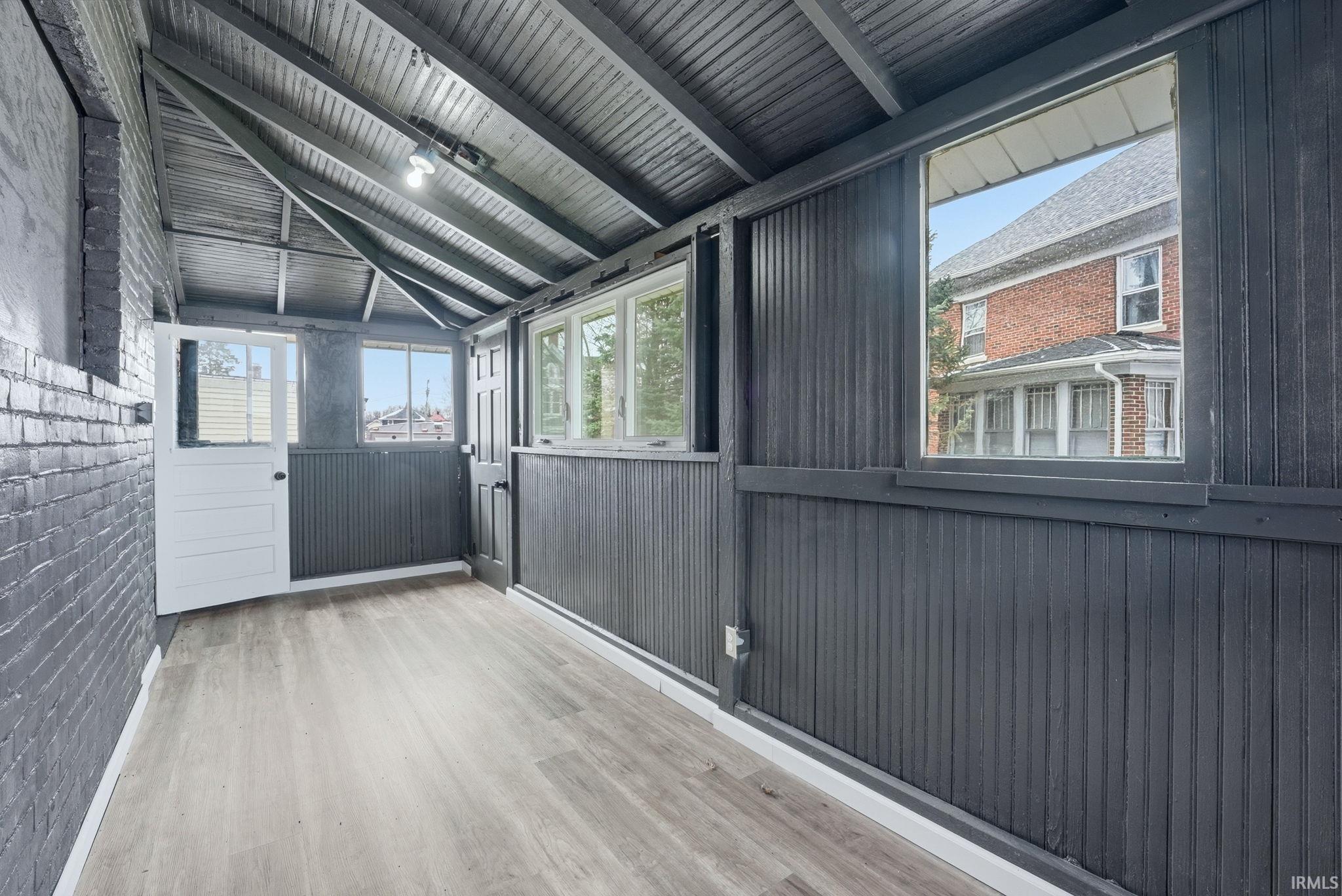 Enclosed porch featuring wood-finish flooring, dark paneling, exposed ceiling rafters, and multiple windows