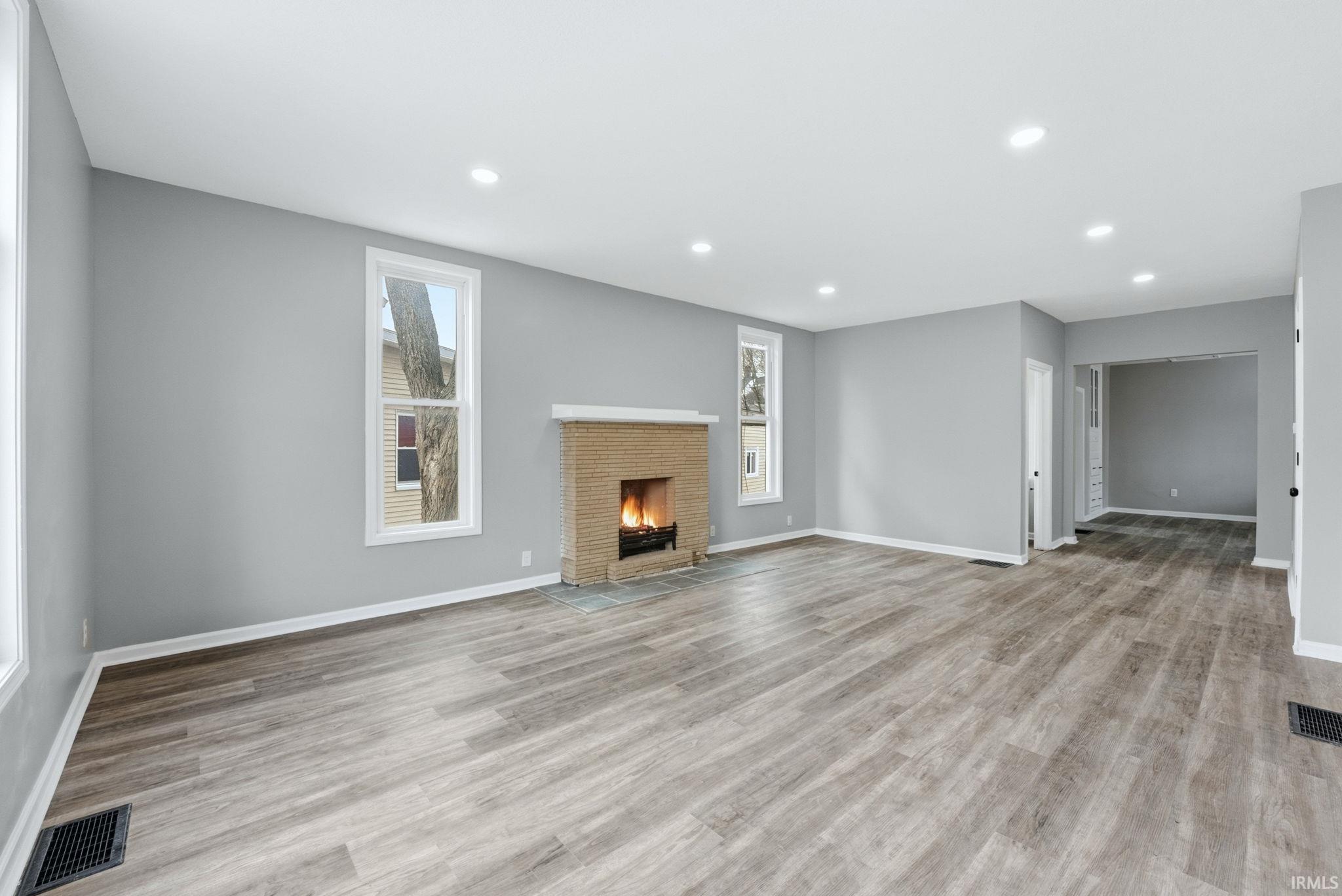 Spacious living area featuring a brick fireplace, recessed lighting, and wood-finish flooring
