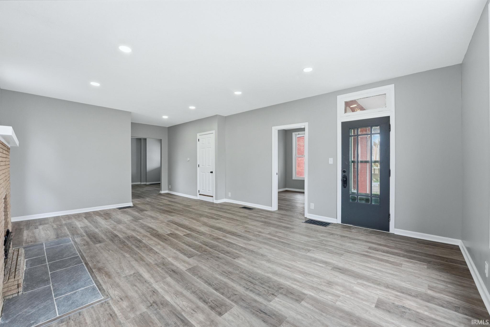 Spacious living area featuring wood-finish flooring, recessed lighting, and a brick fireplace with a tile hearth