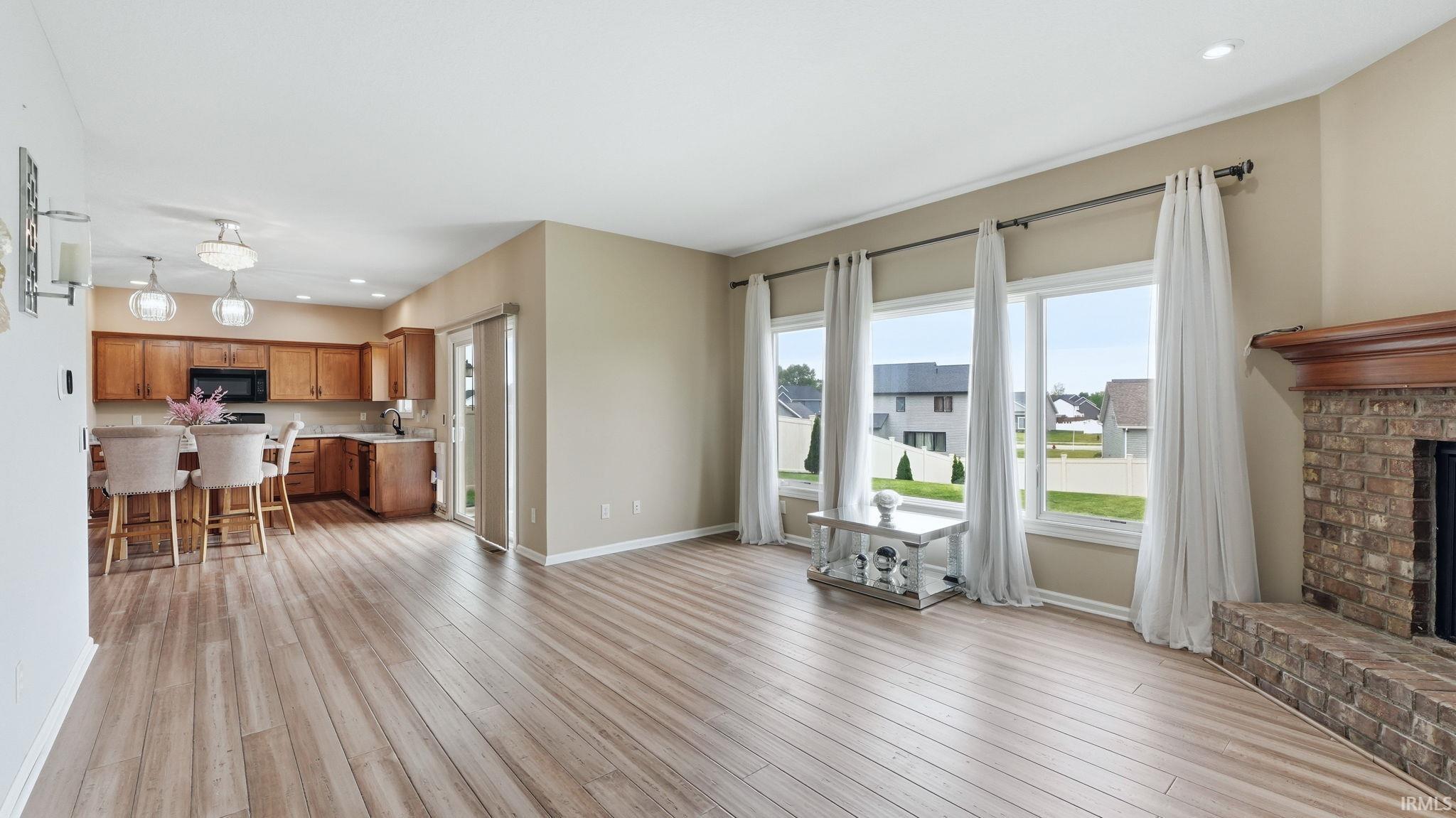 Expansive living area featuring wood-finish flooring, a brick fireplace with a wood mantle, and three large windows