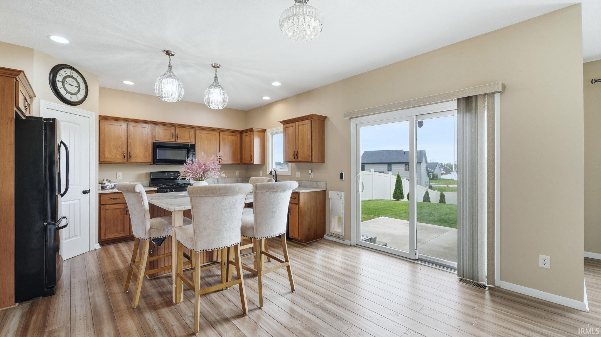 Open-concept kitchen featuring wood-finish flooring, a central island with integrated seating, recessed lighting, and sliding glass doors opening to a concrete patio and green space