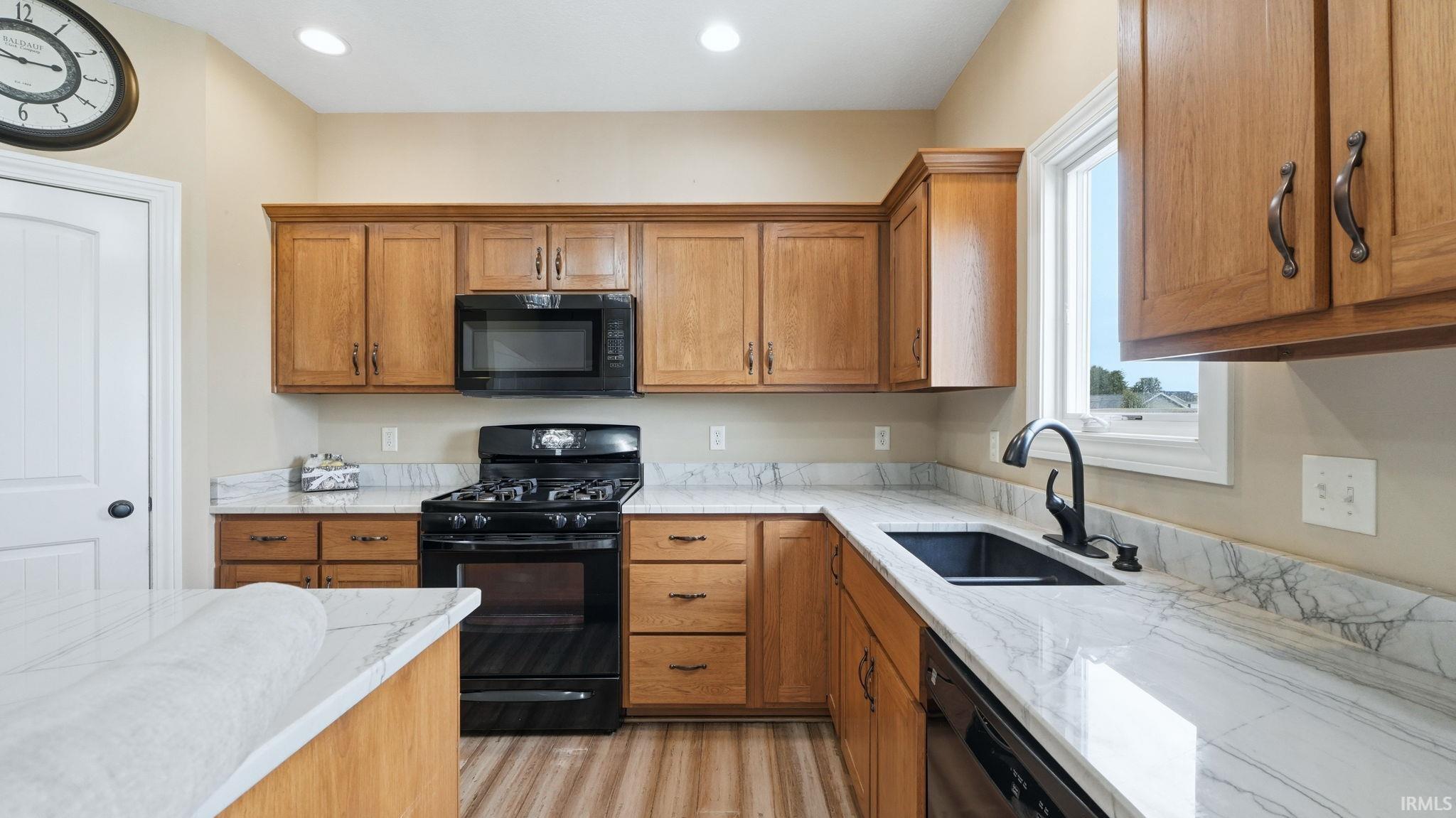 Kitchen featuring wood cabinetry, white countertops with veining, a black gas range, a black microwave, and a black sink with a gooseneck faucet