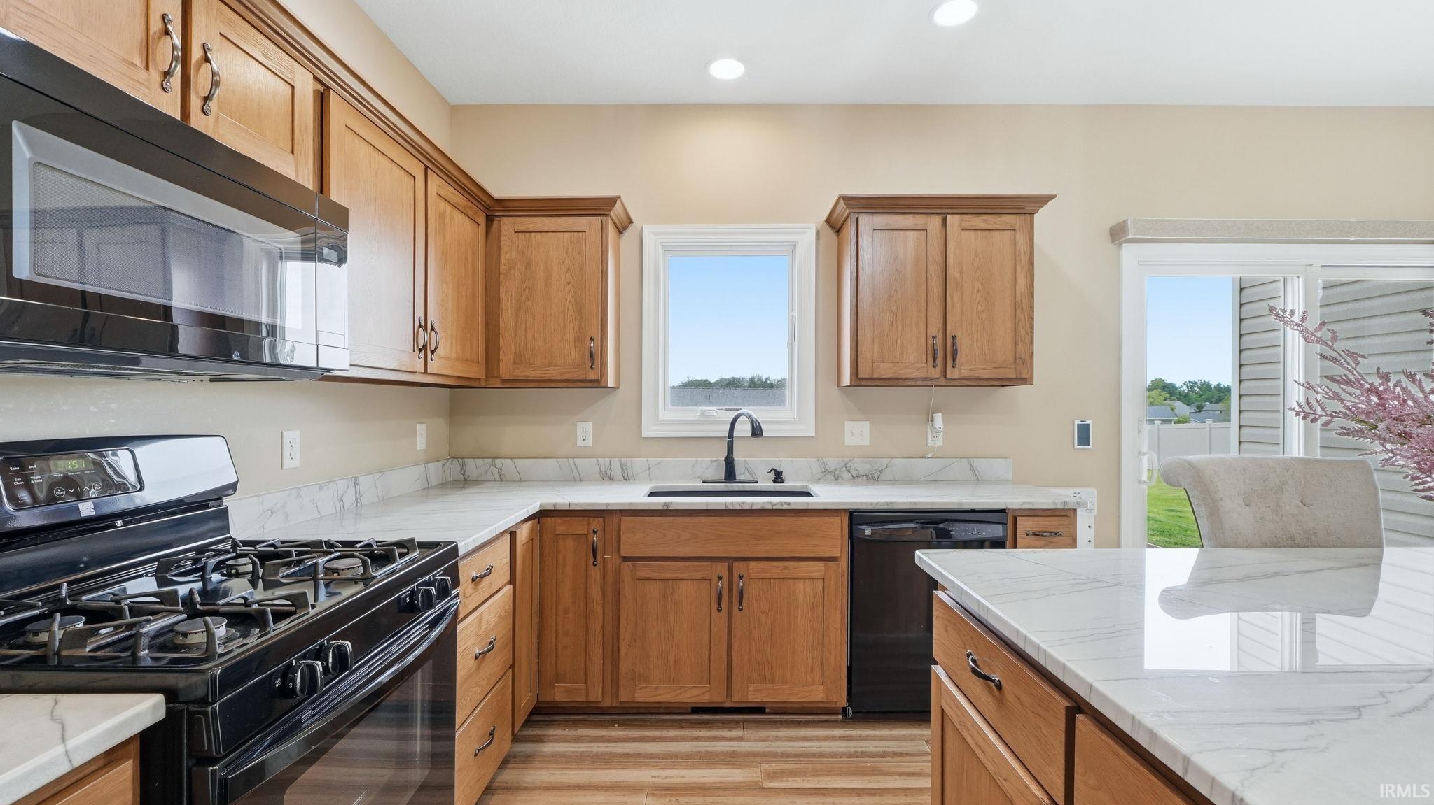Kitchen featuring wood cabinetry, white marble-look countertops, black gas range, black built-in microwave, and black dishwasher