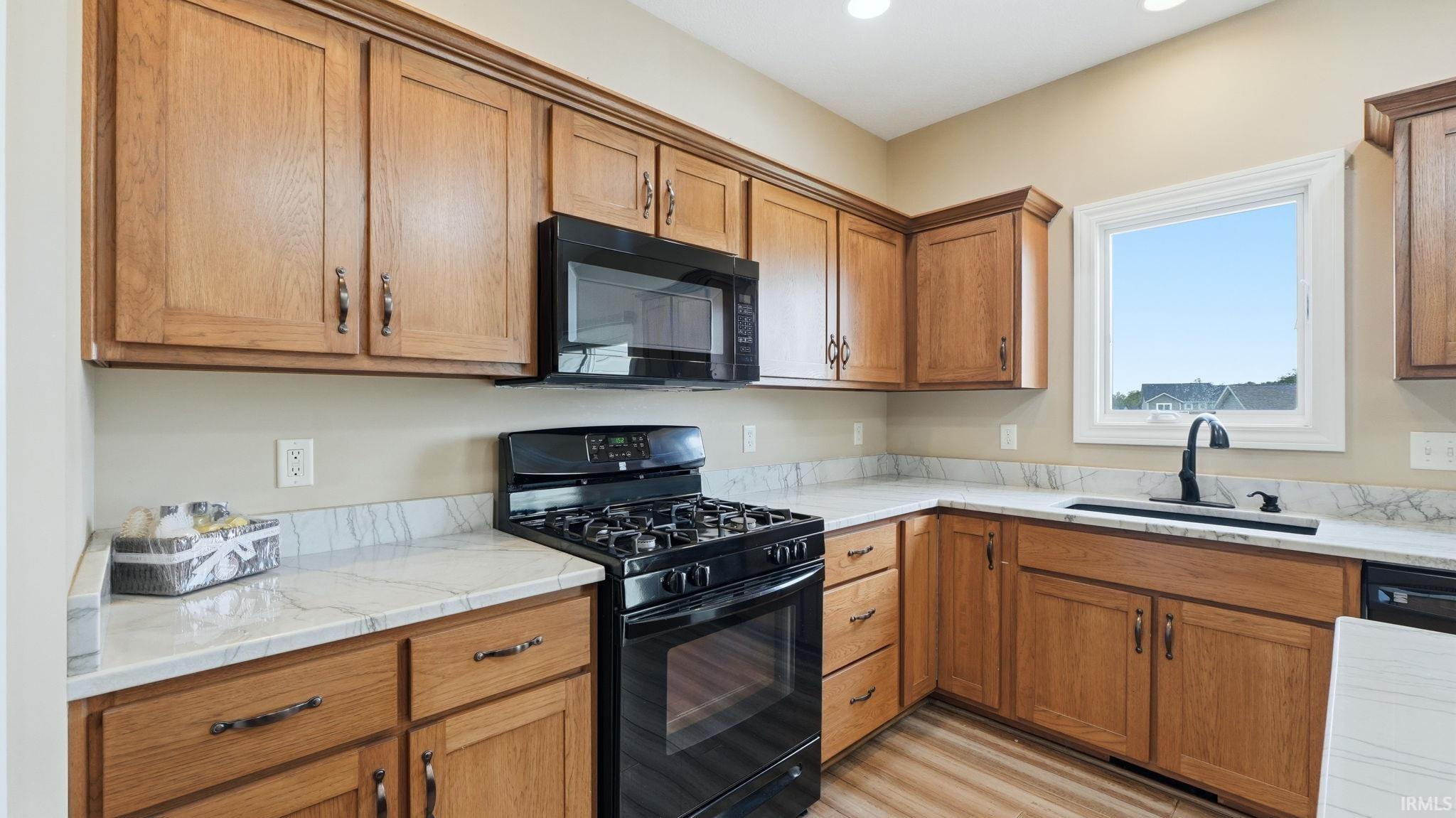 Kitchen featuring wood cabinetry, white countertops with veining, a black gas range, an over-range microwave, and a window with a black faucet
