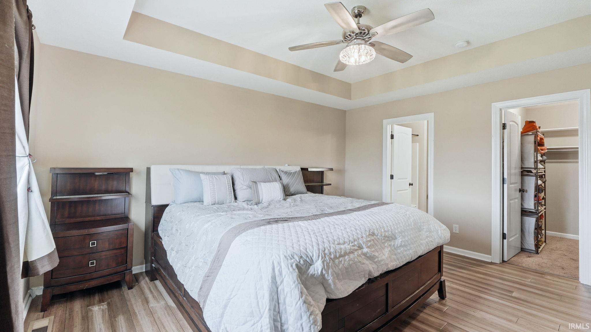 Spacious bedroom featuring wood-finish flooring, a tray ceiling, and a ceiling fan with integrated lighting