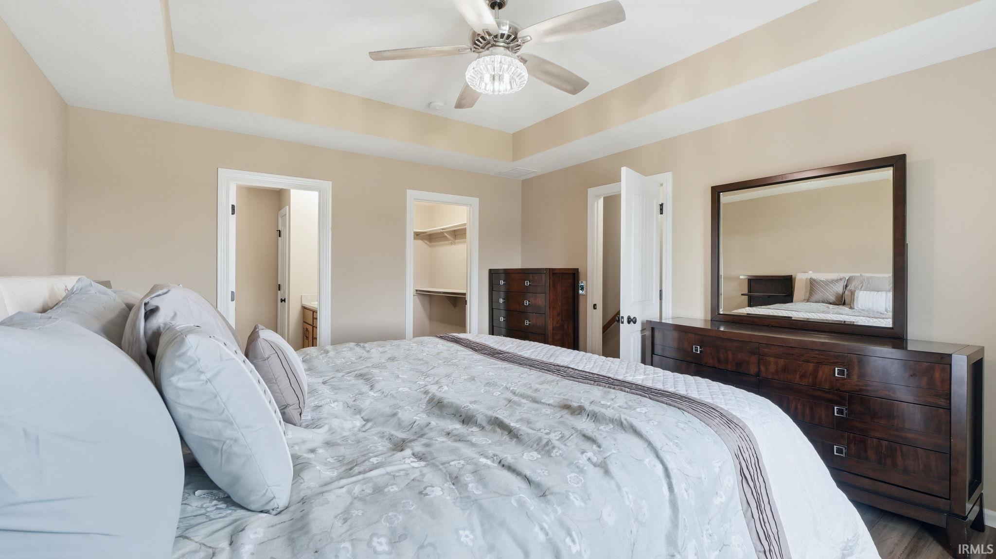 Tray ceiling with a crystal chandelier ceiling fan, neutral wall tones, and dark wood-finish flooring