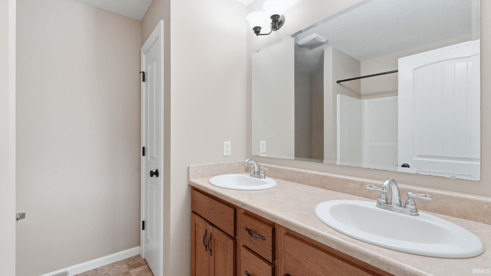 Double vanity with laminate countertop, dual sinks, wood-finish cabinetry, and brushed nickel hardware