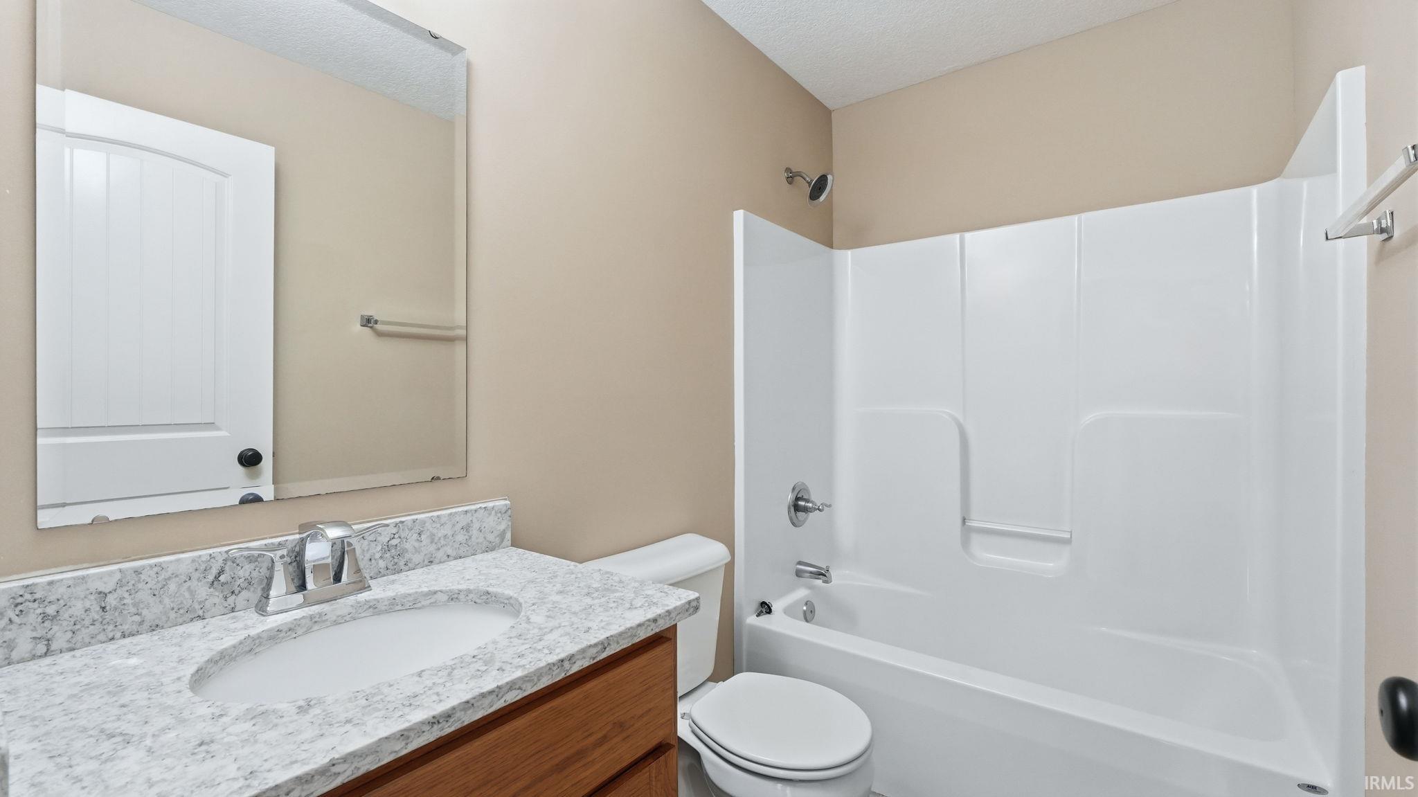 Bathroom featuring a white integrated tub and shower unit, a vanity with a light-colored speckled countertop, an undermount sink, and a chrome faucet