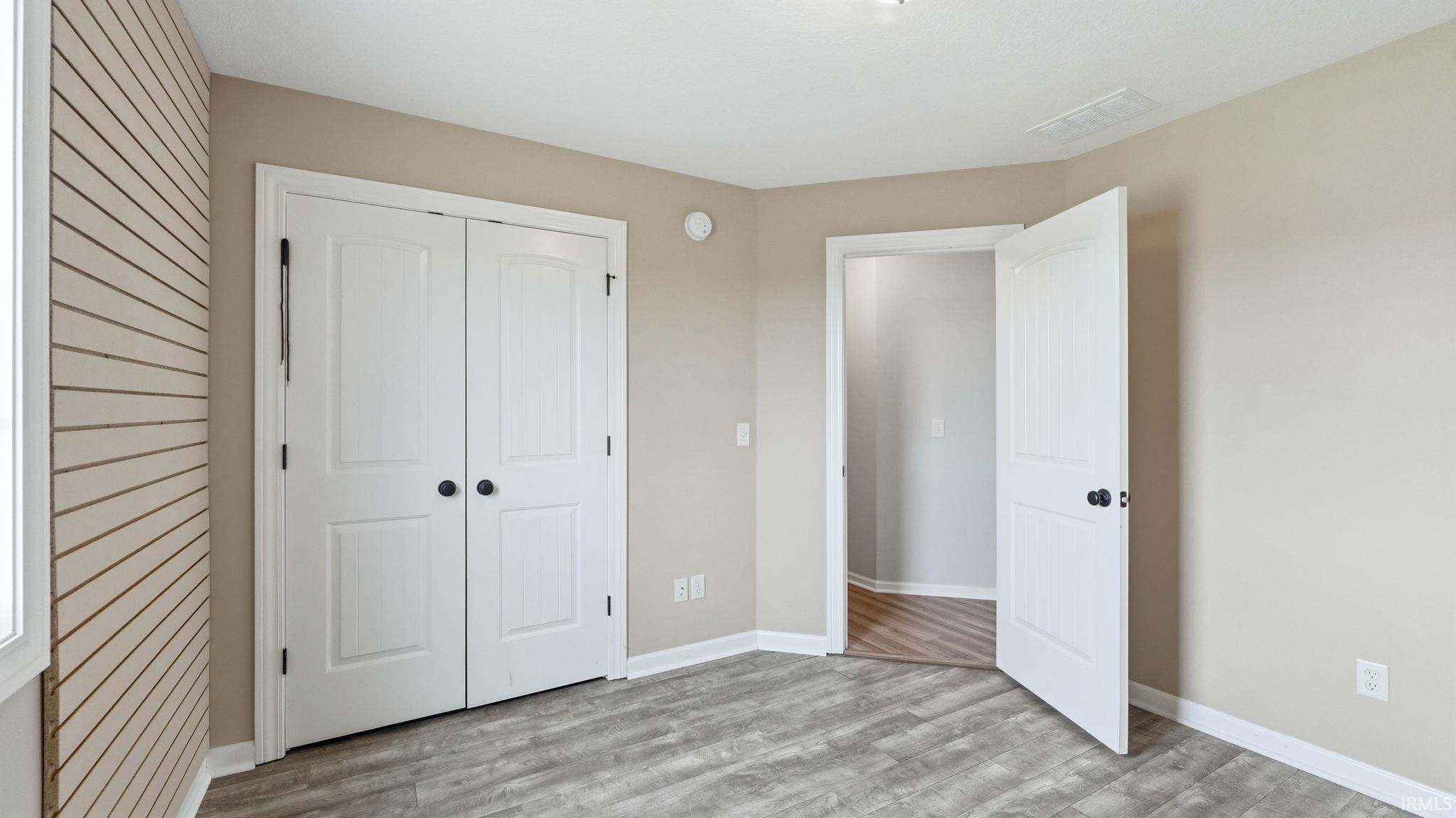 Room featuring light-toned walls, wood-finish flooring, a shiplap accent wall, and white bi-fold closet doors with black hardware