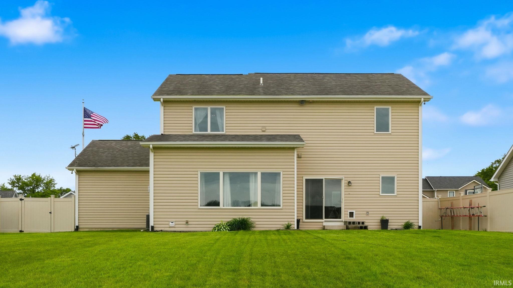 Expansive rear elevation featuring beige vinyl siding, multiple windows, and a sliding glass door leading to the backyard