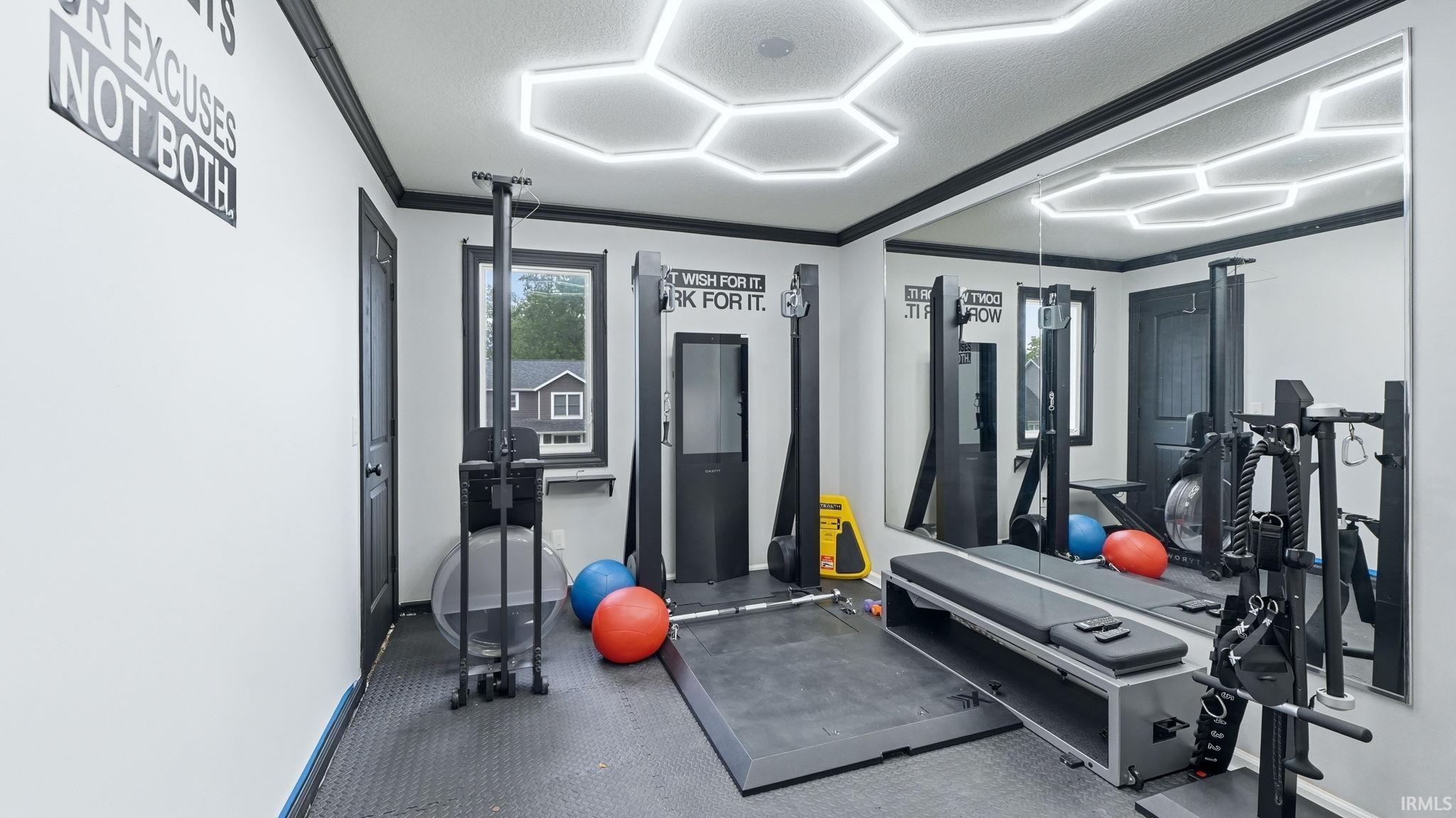 Dedicated fitness space featuring rubber flooring, a full-wall mirror, and hexagonal ceiling lighting