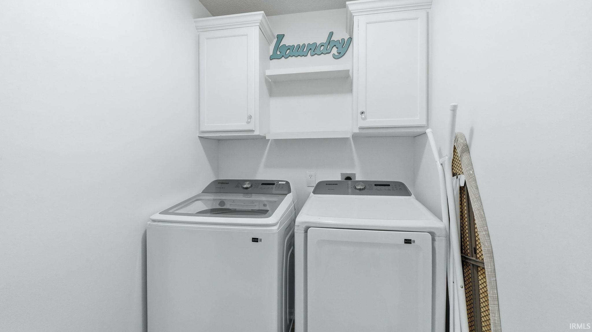 Dedicated laundry area featuring white wall cabinetry and an open shelf for storage